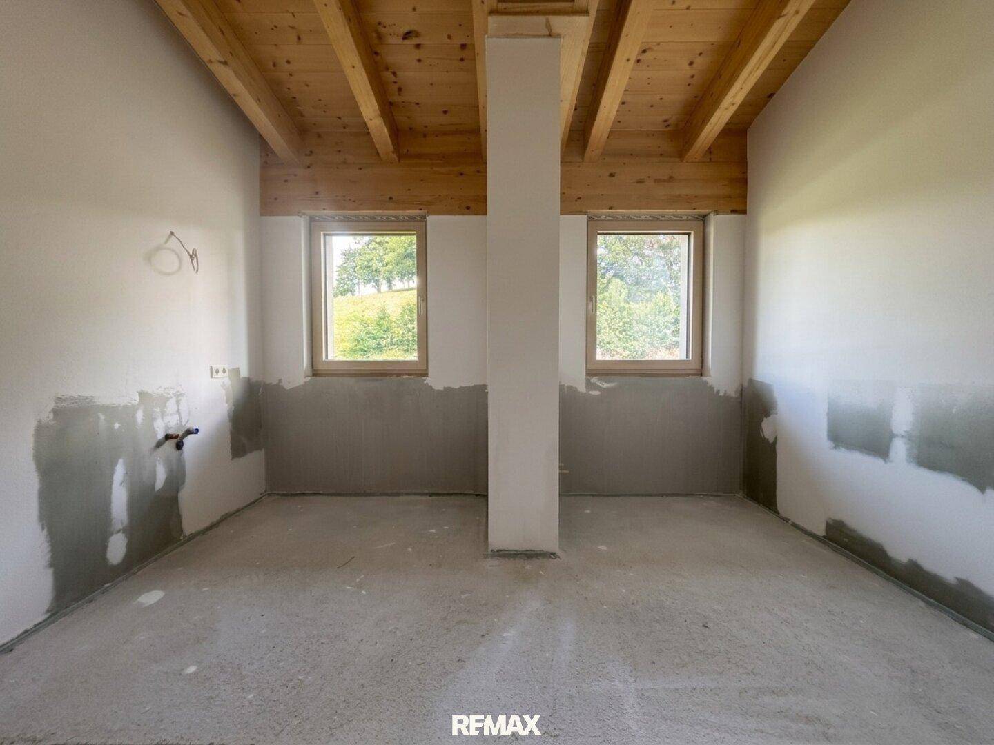 Unmöblierter Raum mit zwei Fenstern, Holzbalkendecke und vorbereiteten Anschlüssen, ideal als Hauswirtschaftsraum.