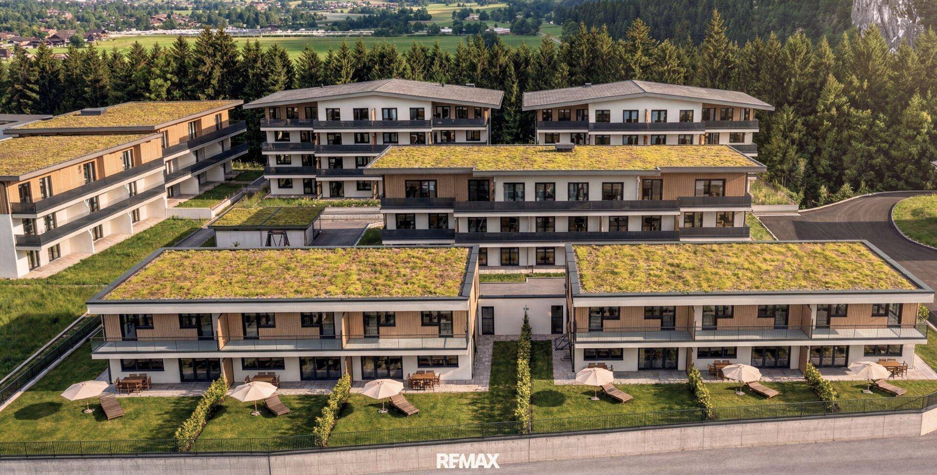 Moderne Wohnanlage mit begrünten Dächern, umgeben von Wald und mit Terrassenbereichen.