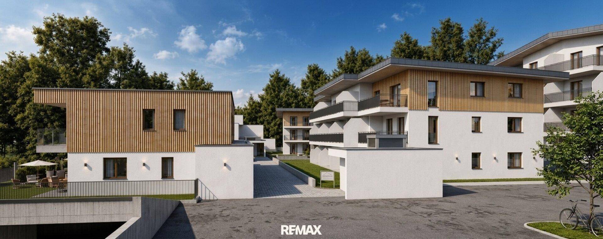 Moderne Wohngebäude mit Holzfassaden und weißem Putz, umgeben von Bäumen und Zufahrtswegen.