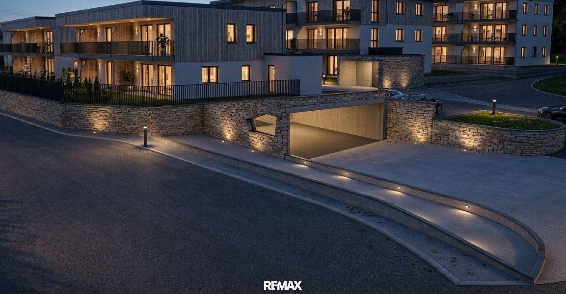 Beleuchtete moderne Wohnanlage bei Nacht mit Tiefgaragenzufahrt und Natursteinmauern.
