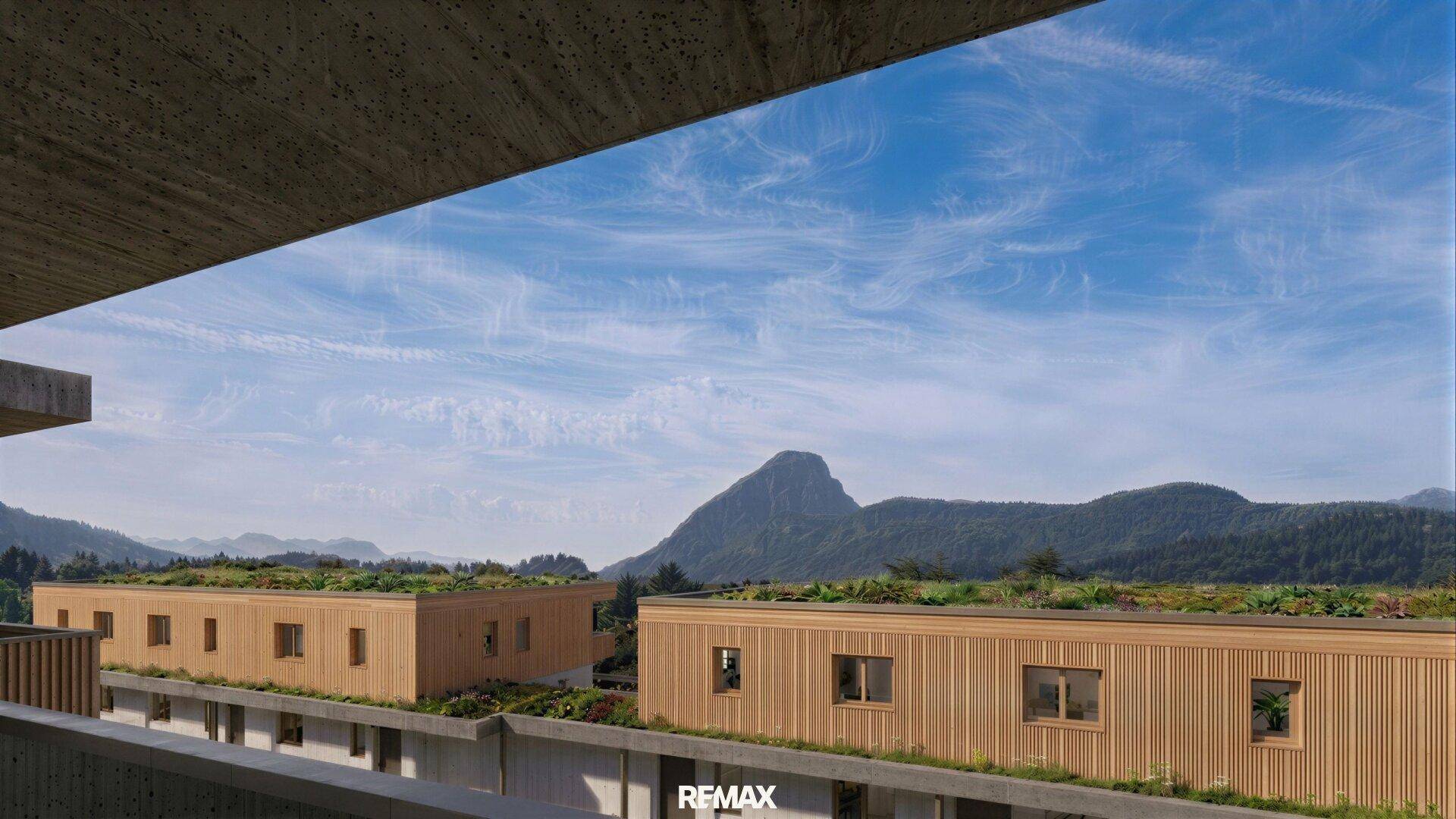 Weitblick von einem Balkon auf moderne Gebäude mit begrünten Dächern und eine beeindruckende Berglandschaft.