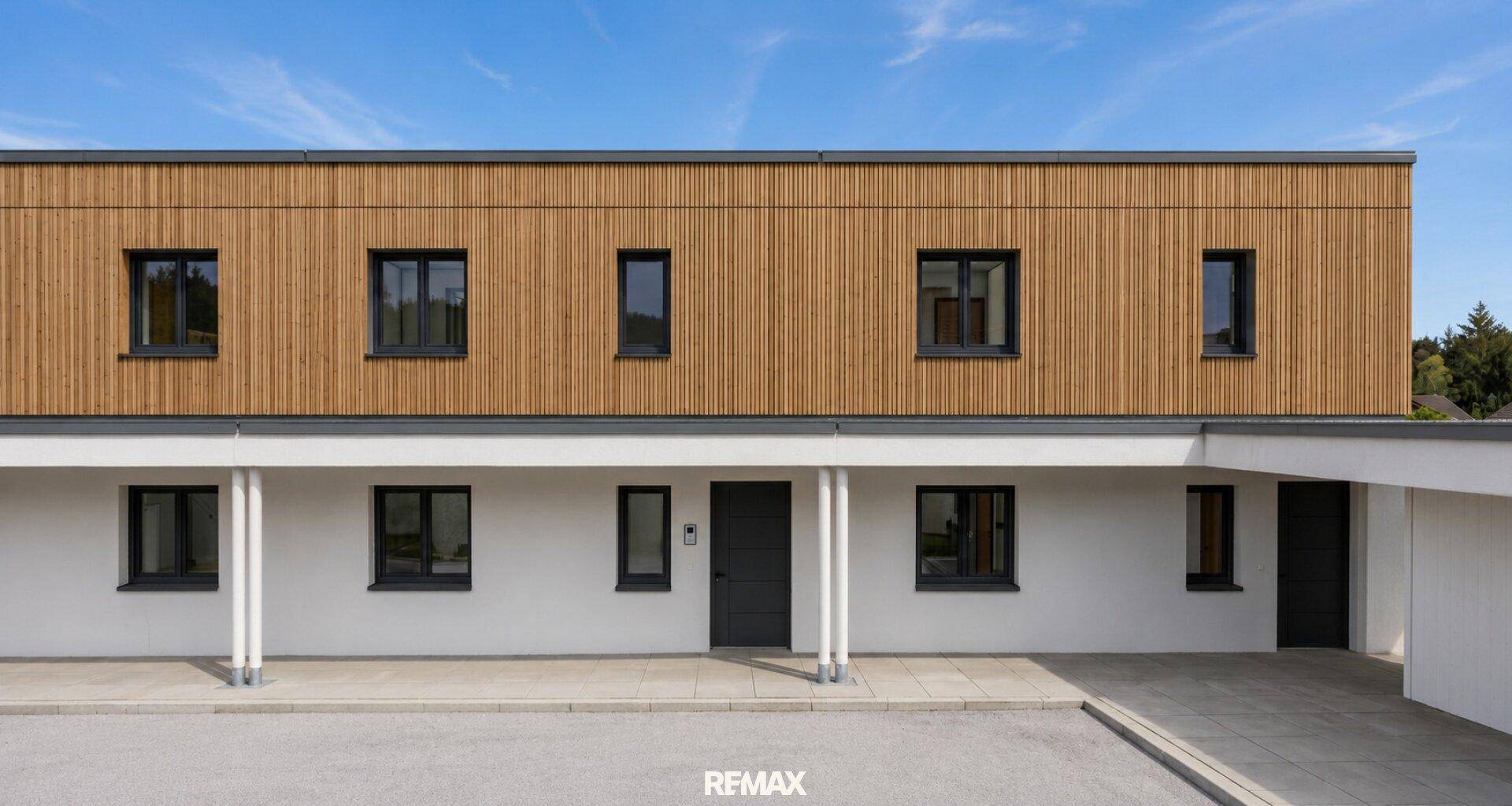 Klare Fassade eines modernen Gebäudes mit Holzverkleidung, weißen Wänden und dunklen Fenstern.