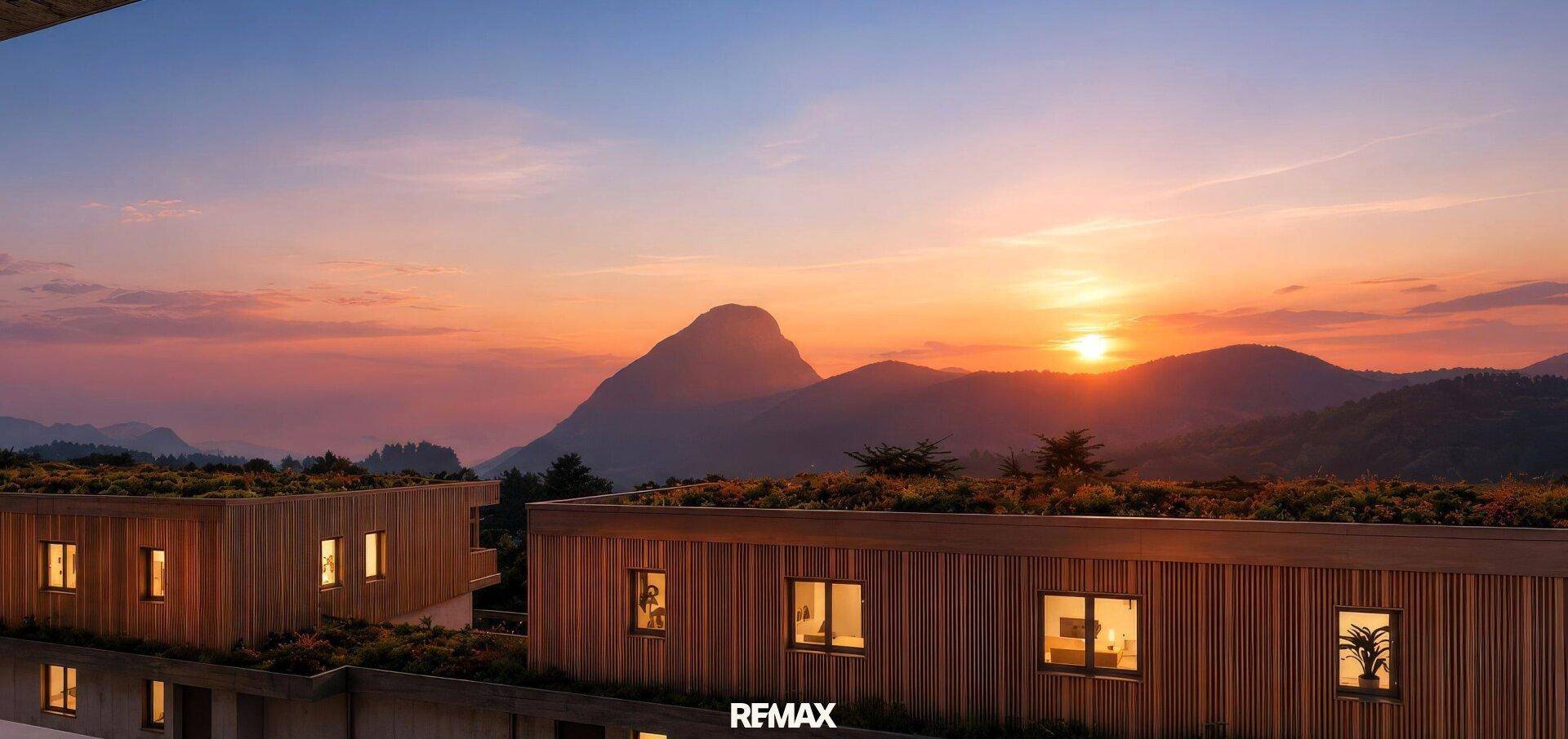 Spektakulärer Sonnenuntergang über modernen Gebäuden mit begrünten Dächern und majestätischer Bergkulisse.