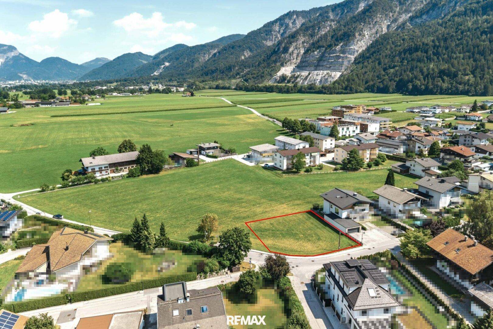 Weitwinkelaufnahme eines Baugrundstücks mit umliegenden Feldern und Bergkulisse.