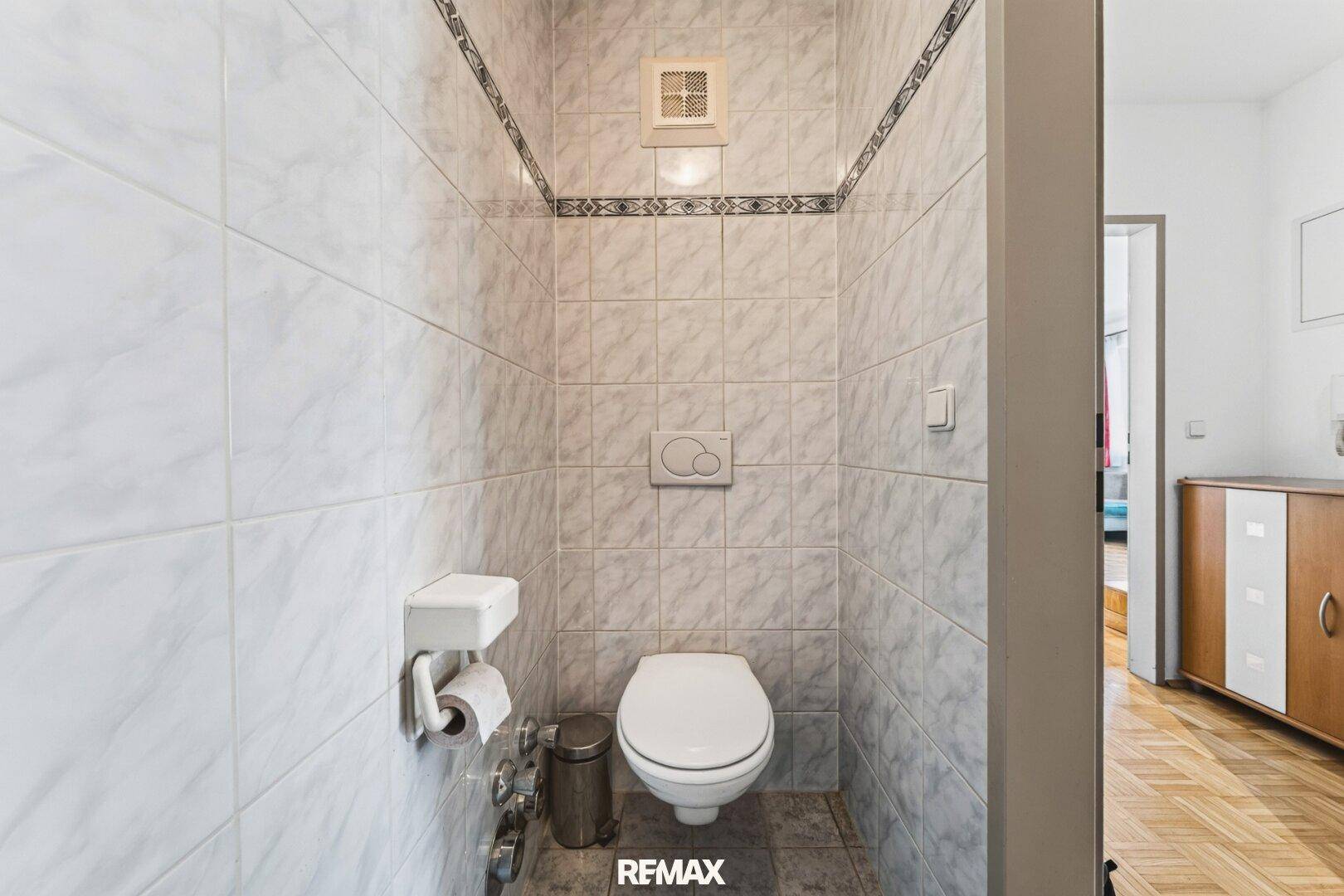 Separate Toilette mit Wand-WC und hellen Fliesen.