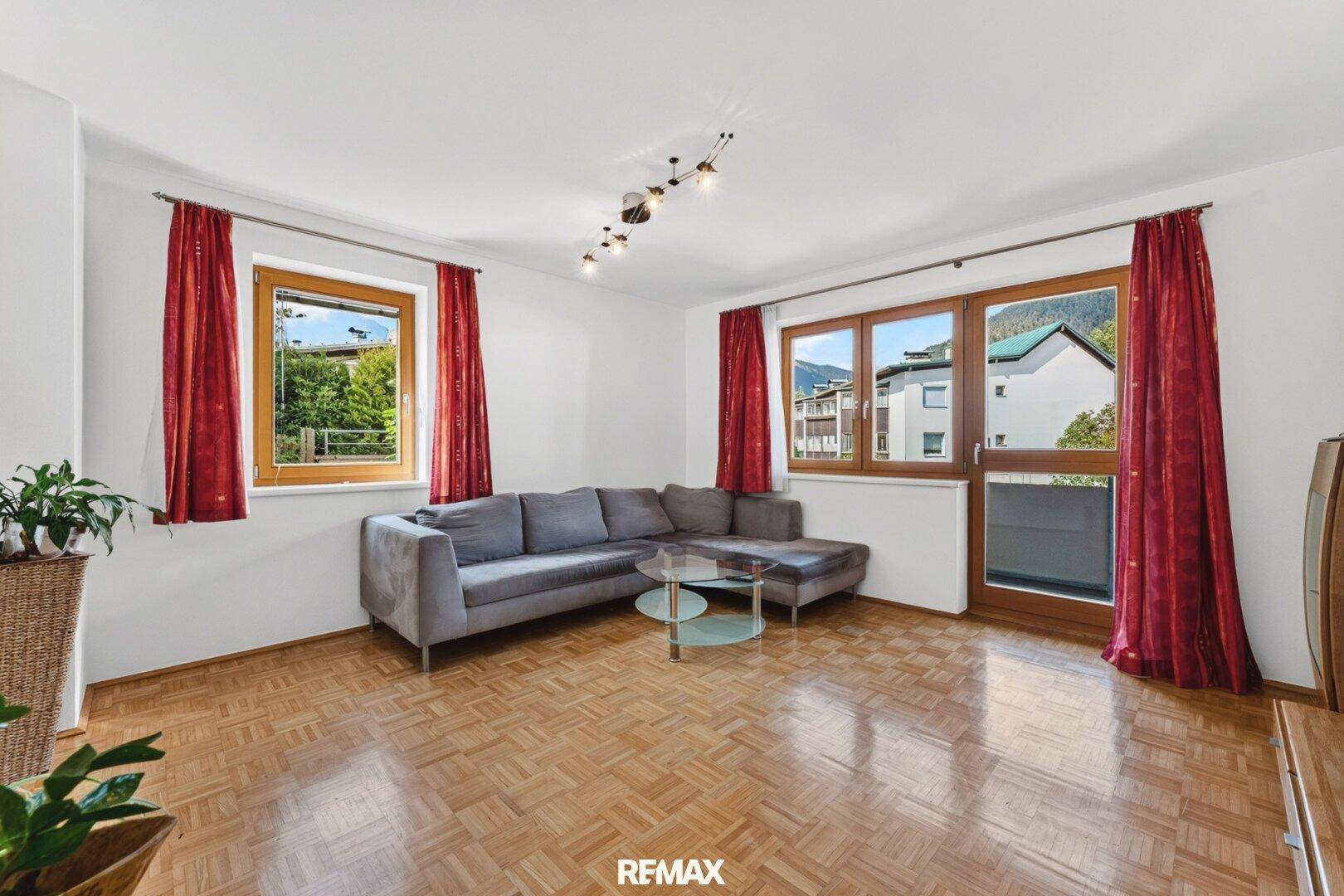 Geräumiges Wohnzimmer mit Parkettboden, großem Ecksofa und Zugang zum Balkon.