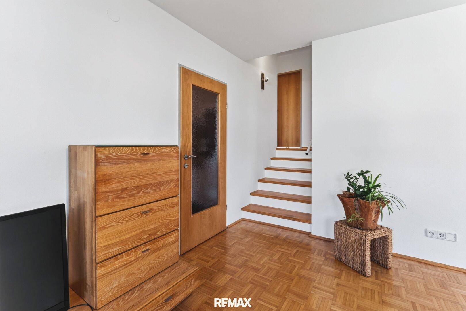 Heller Flurbereich mit Holztreppe, Parkettboden und schlichter Einrichtung.