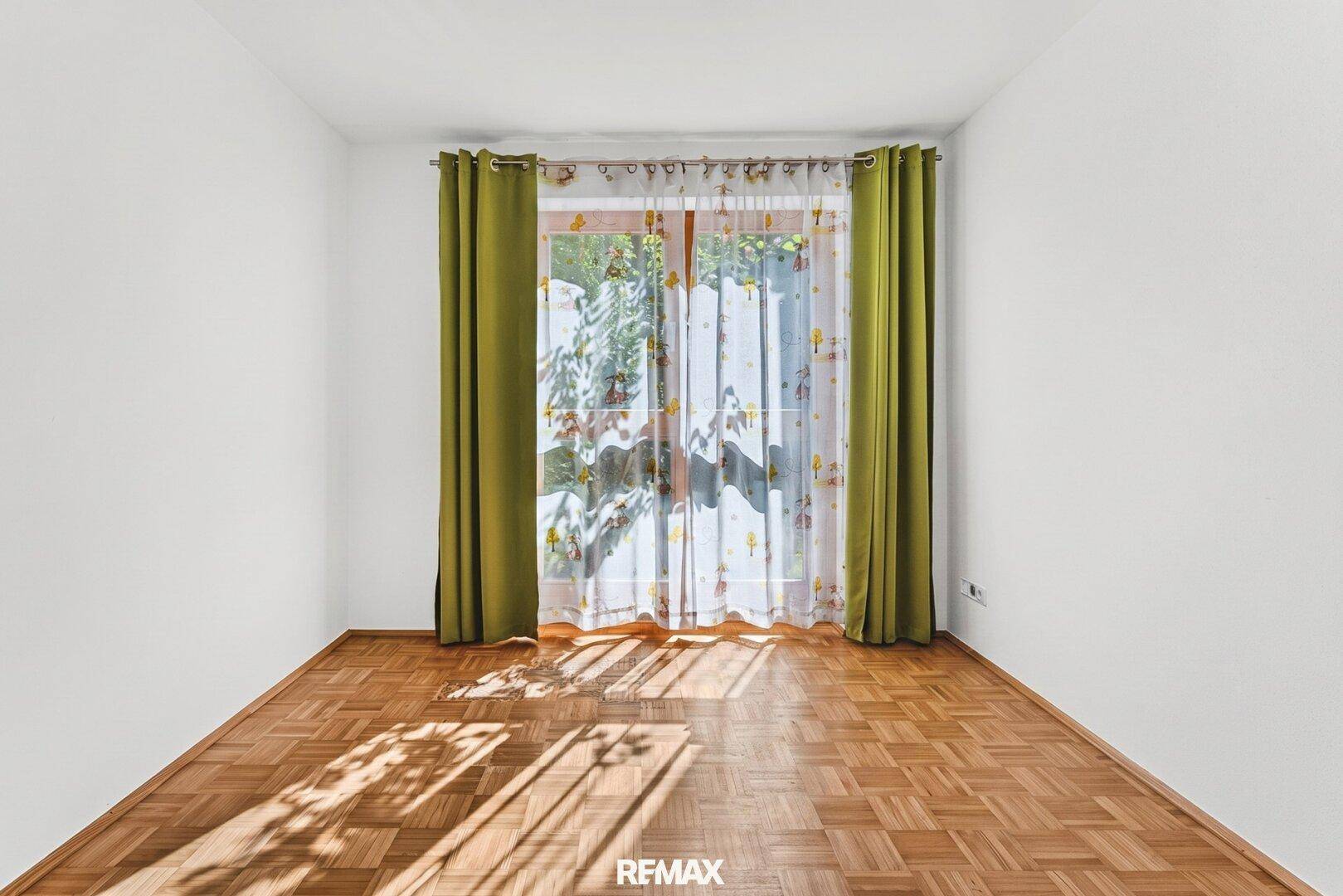 Helles Zimmer mit Parkettboden und großem Fenster, ideal als Schlaf- oder Kinderzimmer.