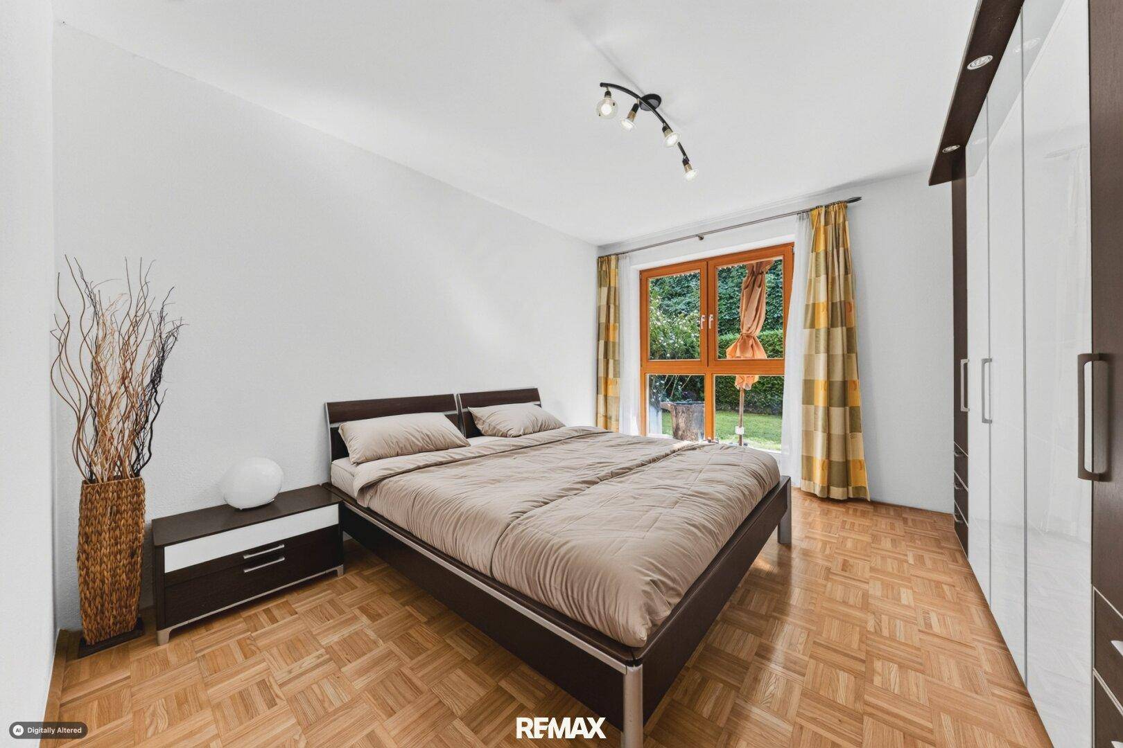 Schlafzimmer mit Doppelbett, Parkettboden und Fenster zum Gartenbereich.