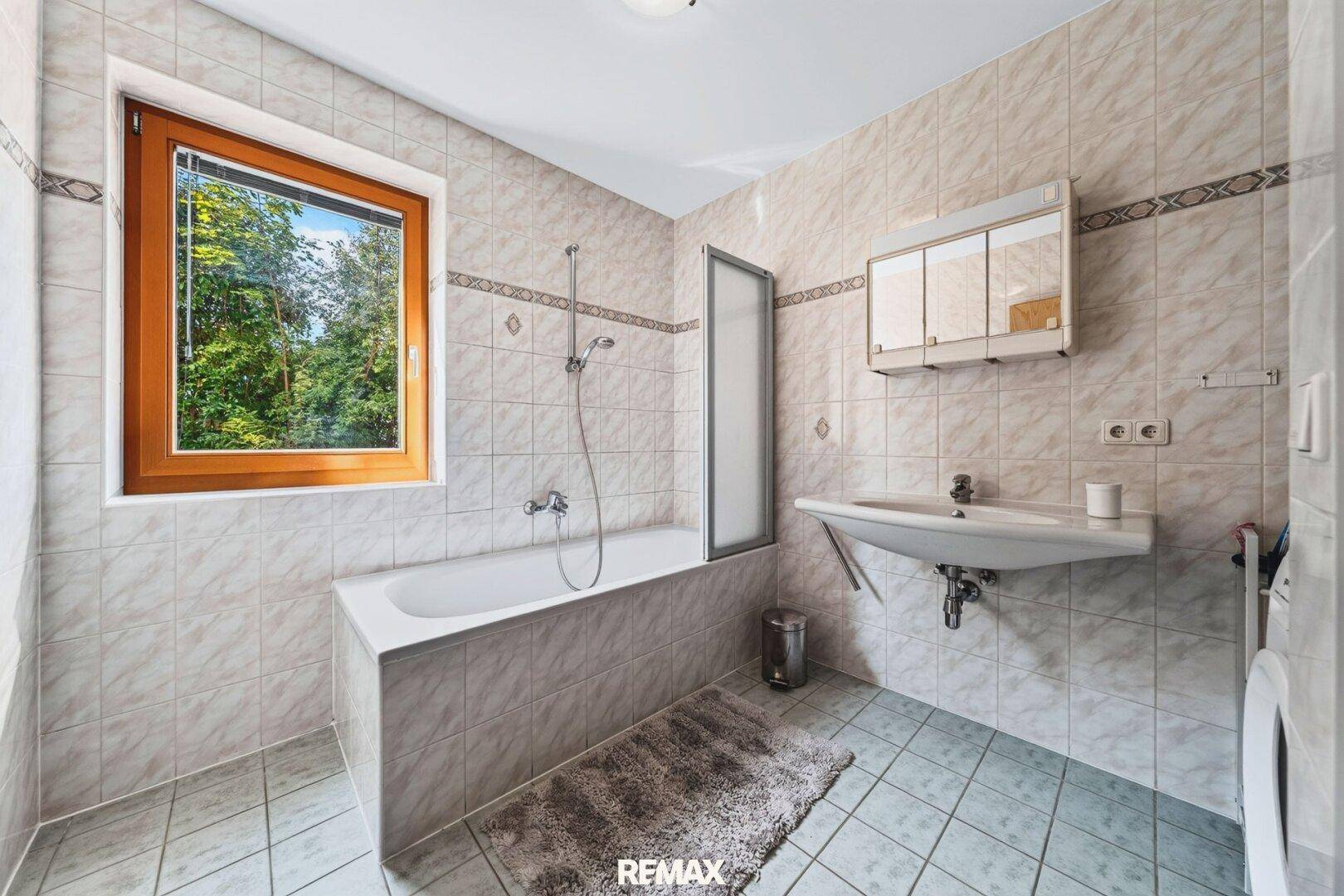 Gefliestes Badezimmer mit Badewanne, Dusche und Fenster für Tageslicht.