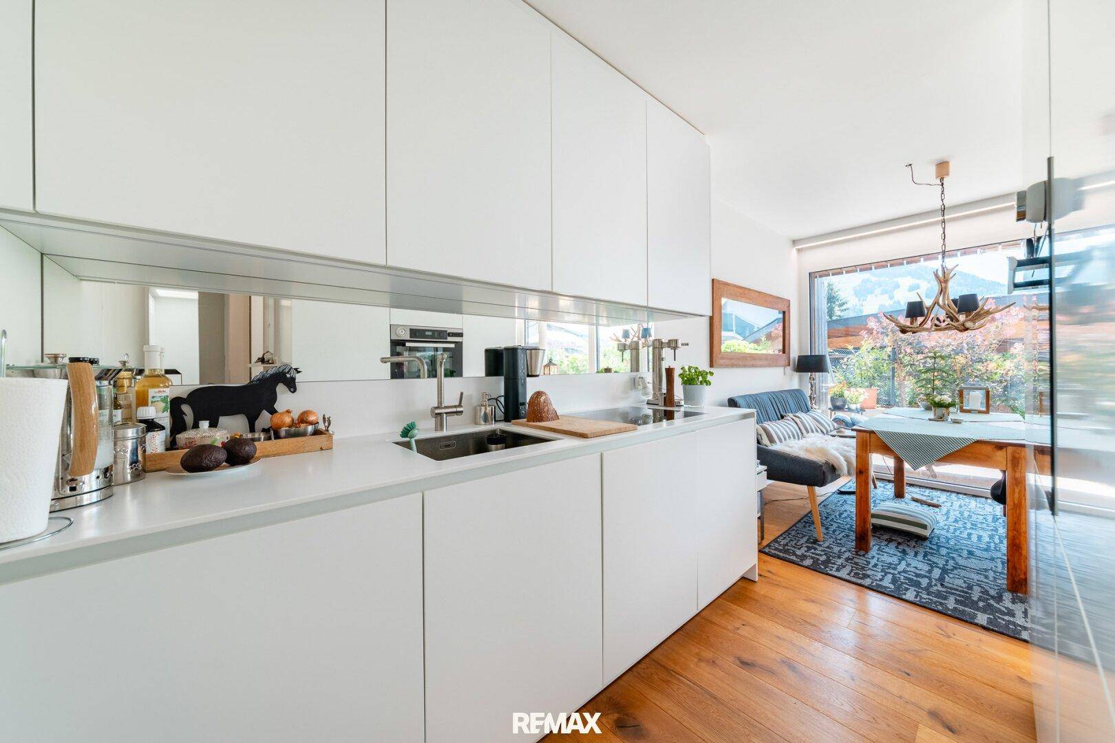 Moderne weiße Küche mit integrierten Geräten und Blick auf den Essbereich und die Terrasse.