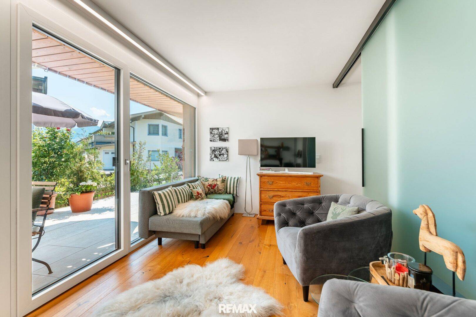 Gemütliches Wohnzimmer mit Holzboden, bequemen Sofas und Zugang zu einer sonnigen Terrasse.