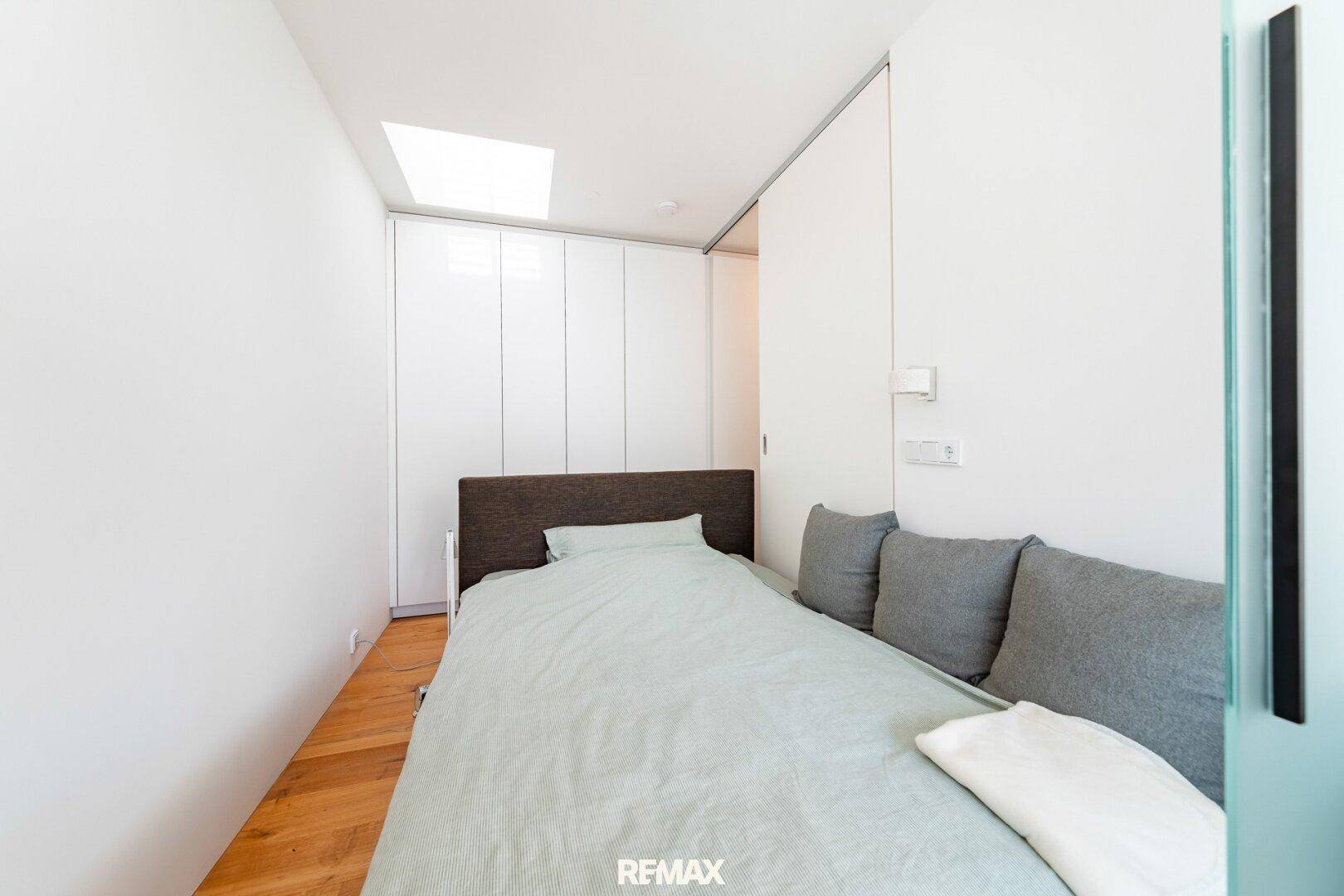 Helles Schlafzimmer mit Einzelbett, Einbauschränken und einem Dachfenster für natürliches Licht.