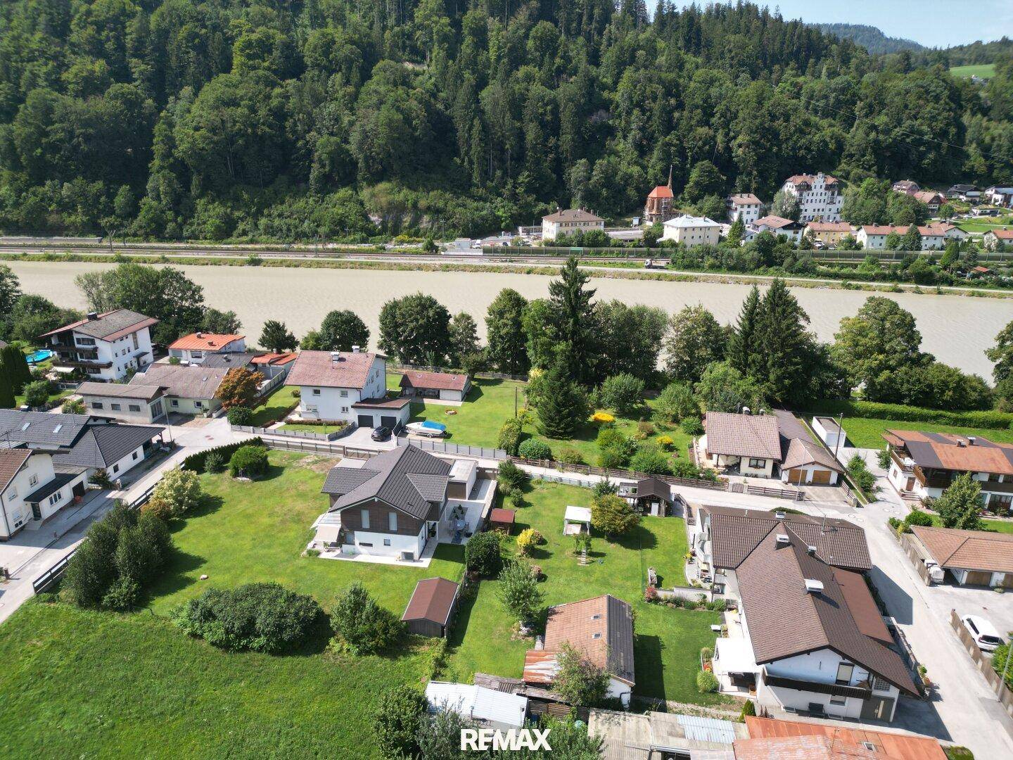 Luftaufnahme eines Wohngebiets mit Fluss, Bergen und einem rot umrandeten Grundstück in ländlicher Umgebung.