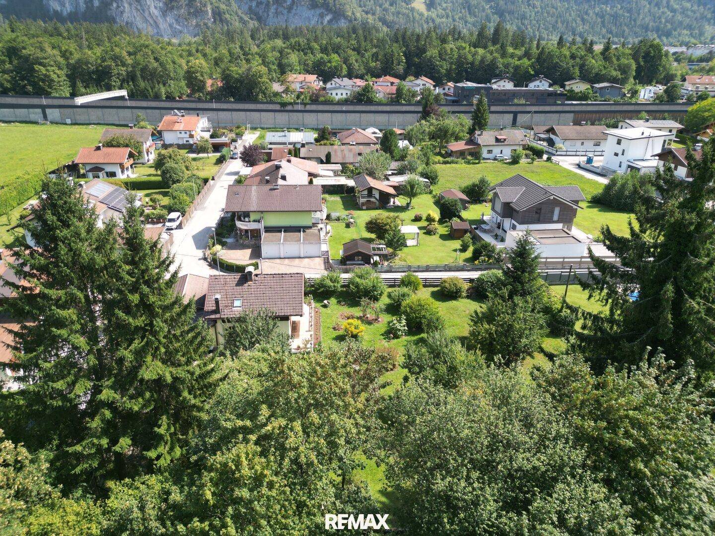 Luftaufnahme eines Wohngebiets, umgeben von Bäumen, mit beeindruckender Bergkulisse im Hintergrund.