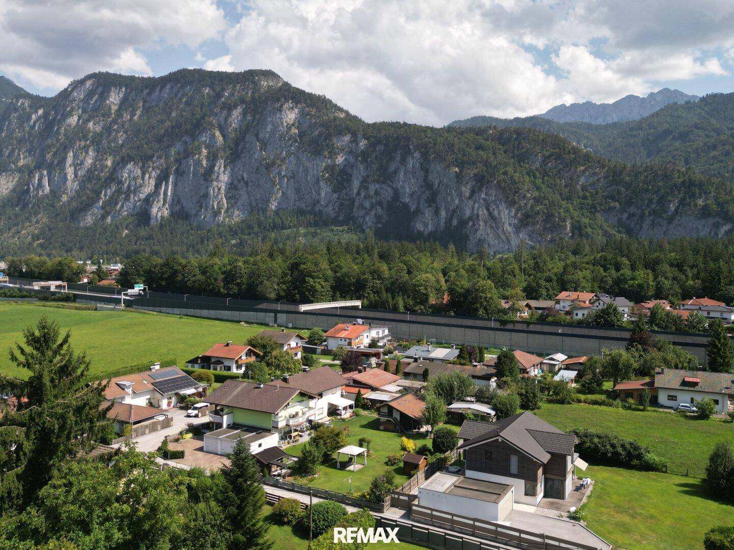 Weitläufige Luftaufnahme eines Wohngebiets mit einer imposanten Bergkette und grünen Feldern.