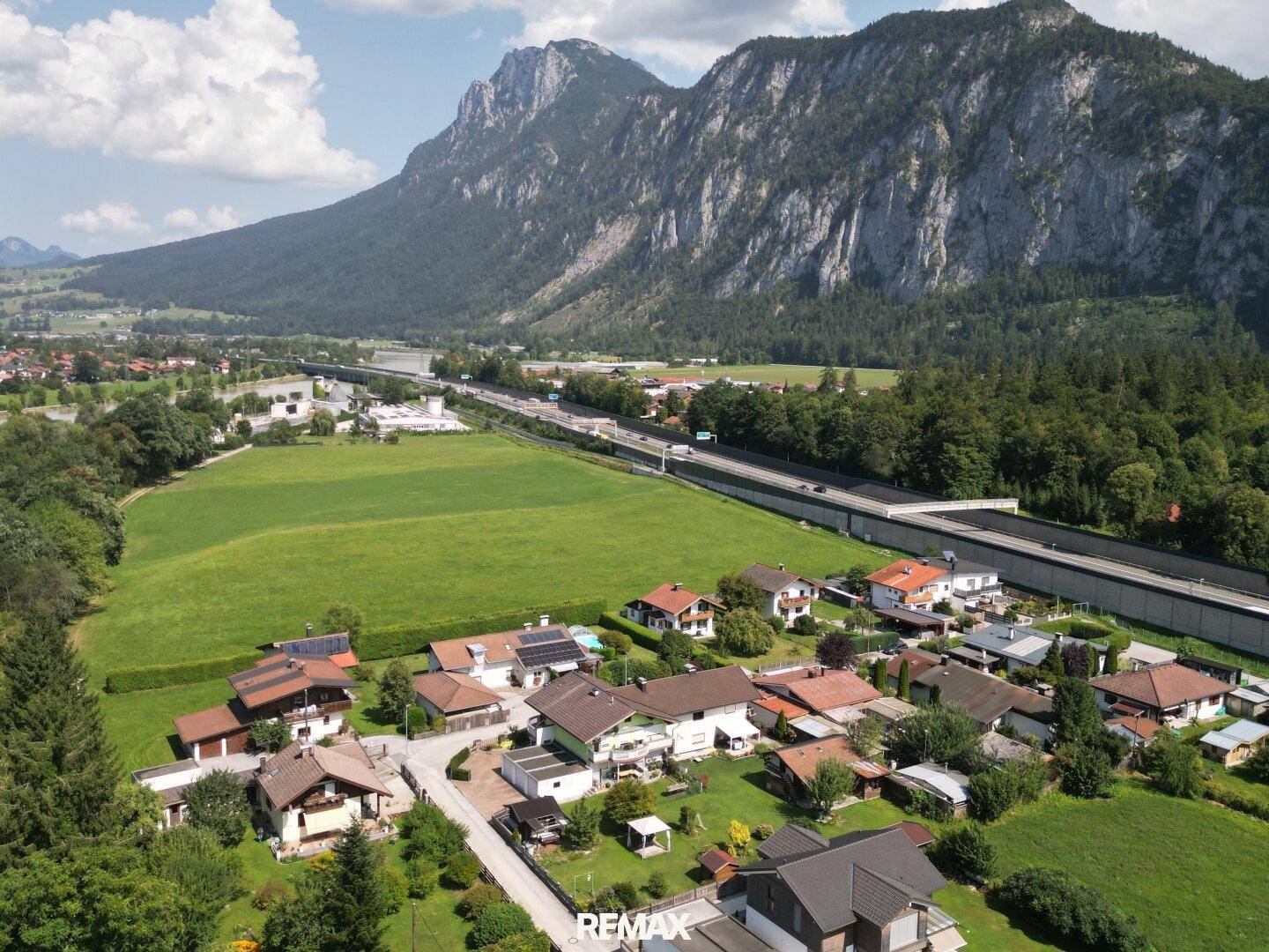 Luftaufnahme eines Wohngebiets mit Autobahn, weiten Feldern und einer majestätischen Berglandschaft.
