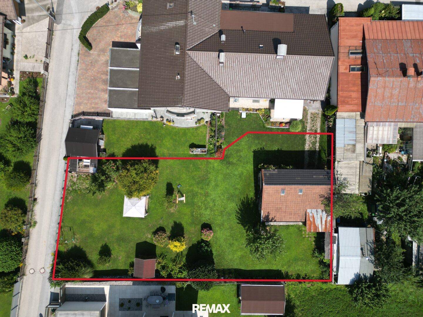 Vogelperspektive des Grundstücks mit großem Rasen, Gartenhaus und angrenzenden Gebäuden, rot umrandet.