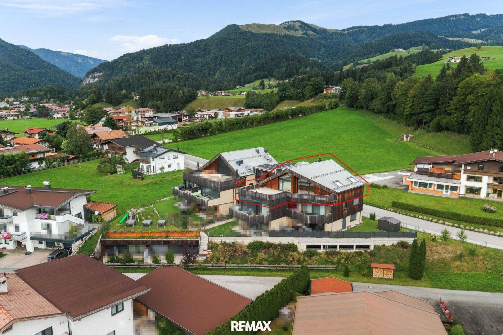 Luftaufnahme eines modernen Wohnkomplexes in alpiner Landschaft mit grünen Hügeln.