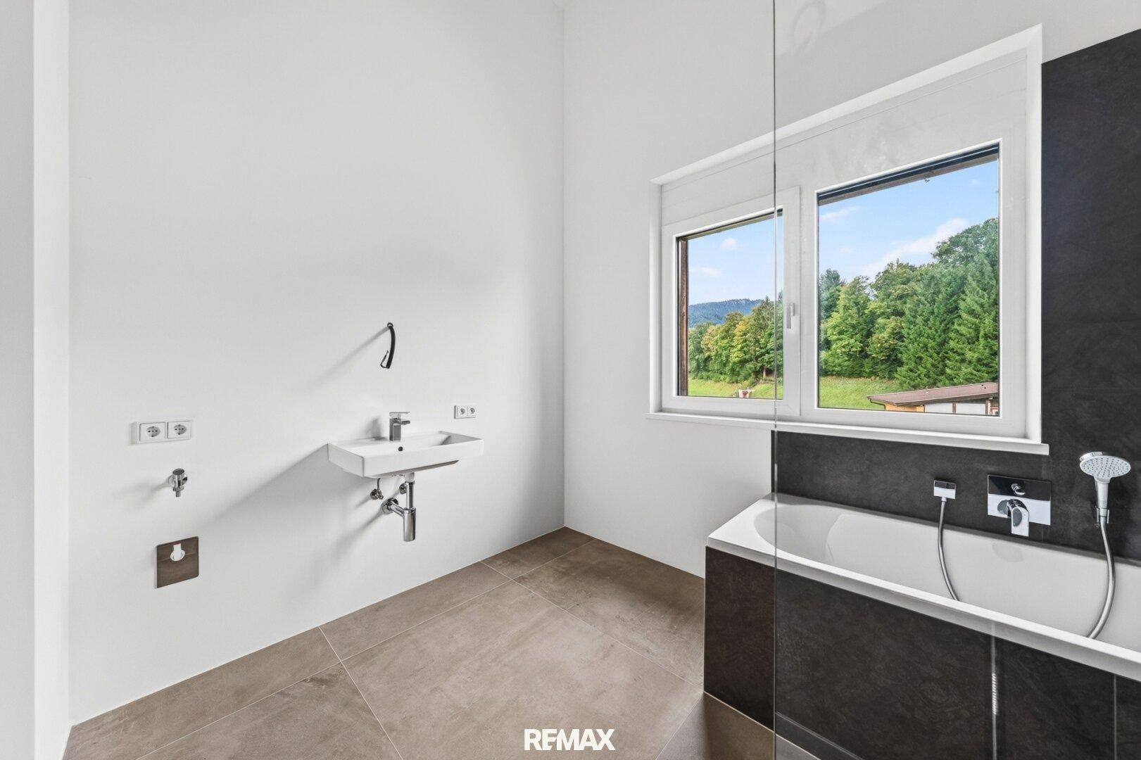 Helles Badezimmer mit modernem Waschbecken, Badewanne und Fenster mit Blick ins Grüne.