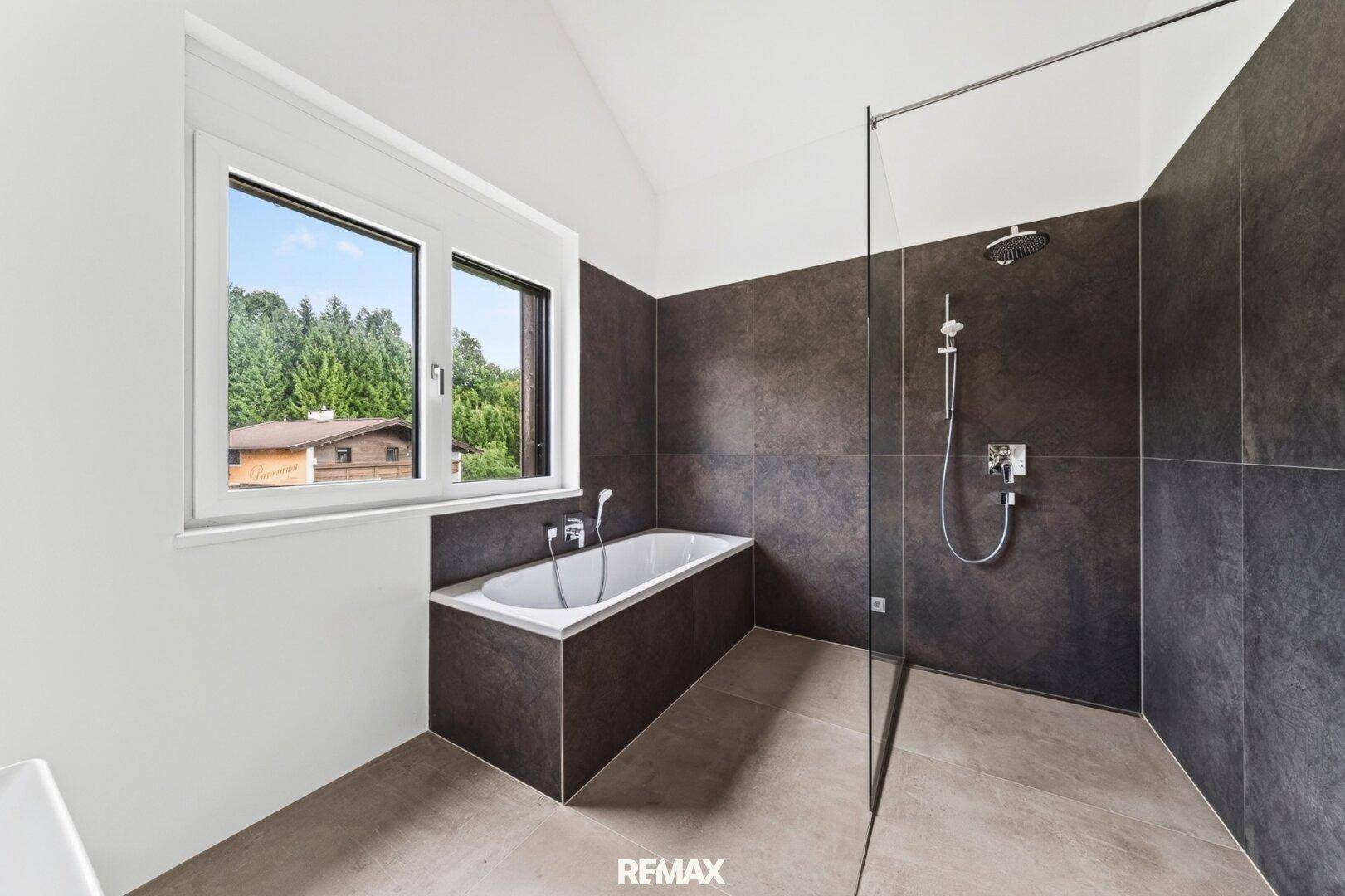 Modernes Badezimmer mit Badewanne, ebenerdiger Dusche und Fenster mit Waldblick.