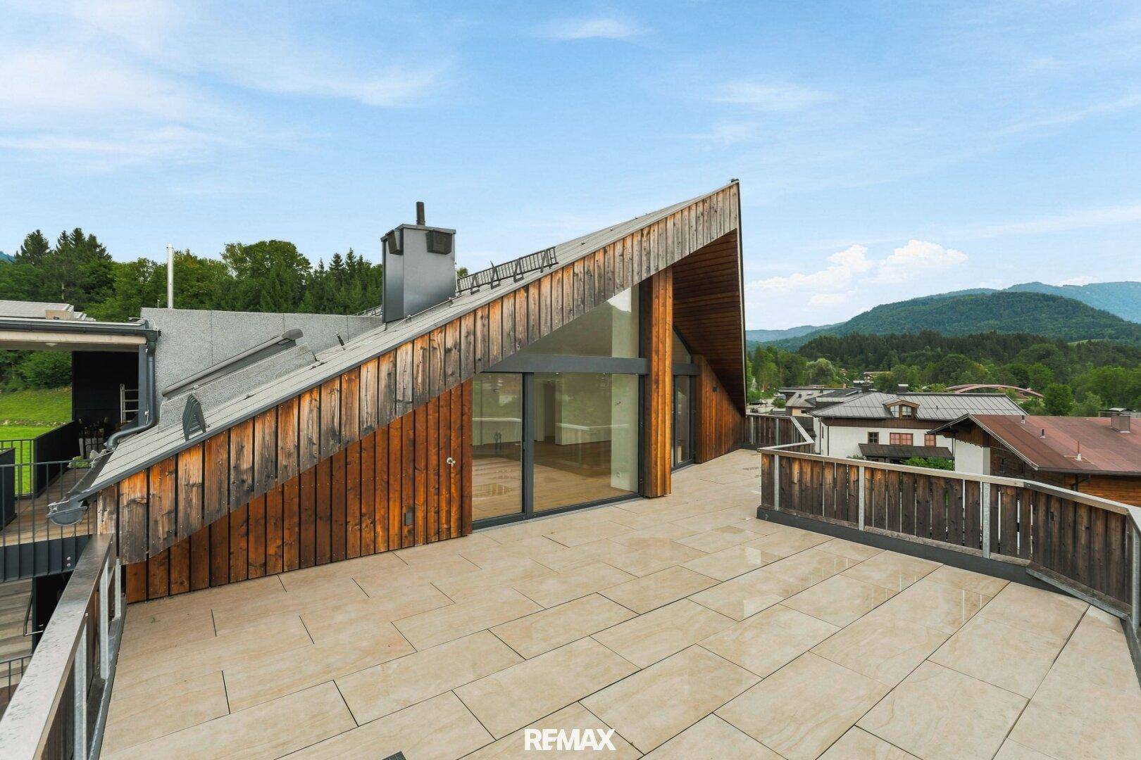 Große Dachterrasse mit Holzfassade und Panoramablick auf die grüne Umgebung und Berge.