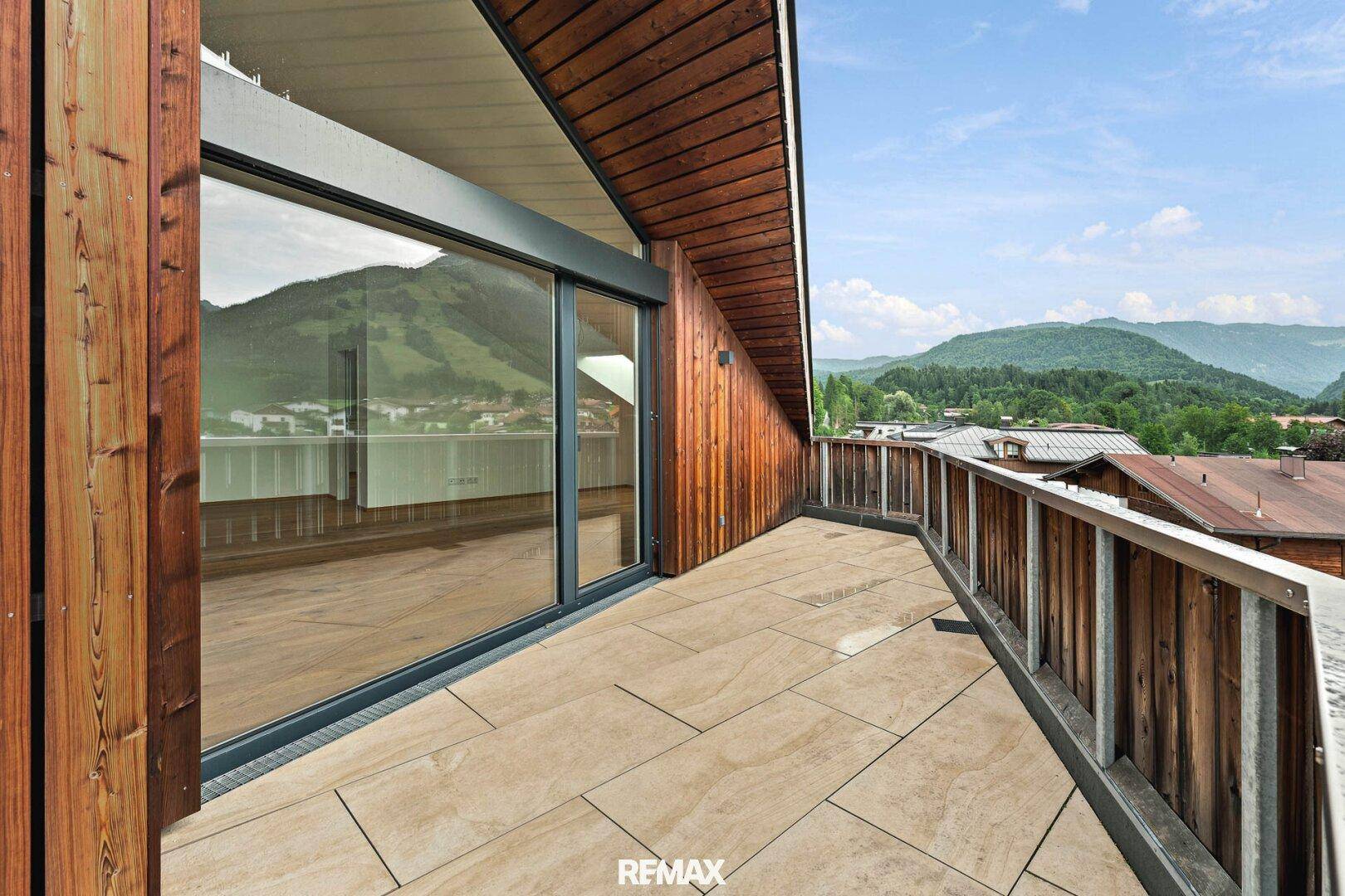 Schmale Terrasse entlang der Holzfassade mit Blick auf die hügelige Landschaft.