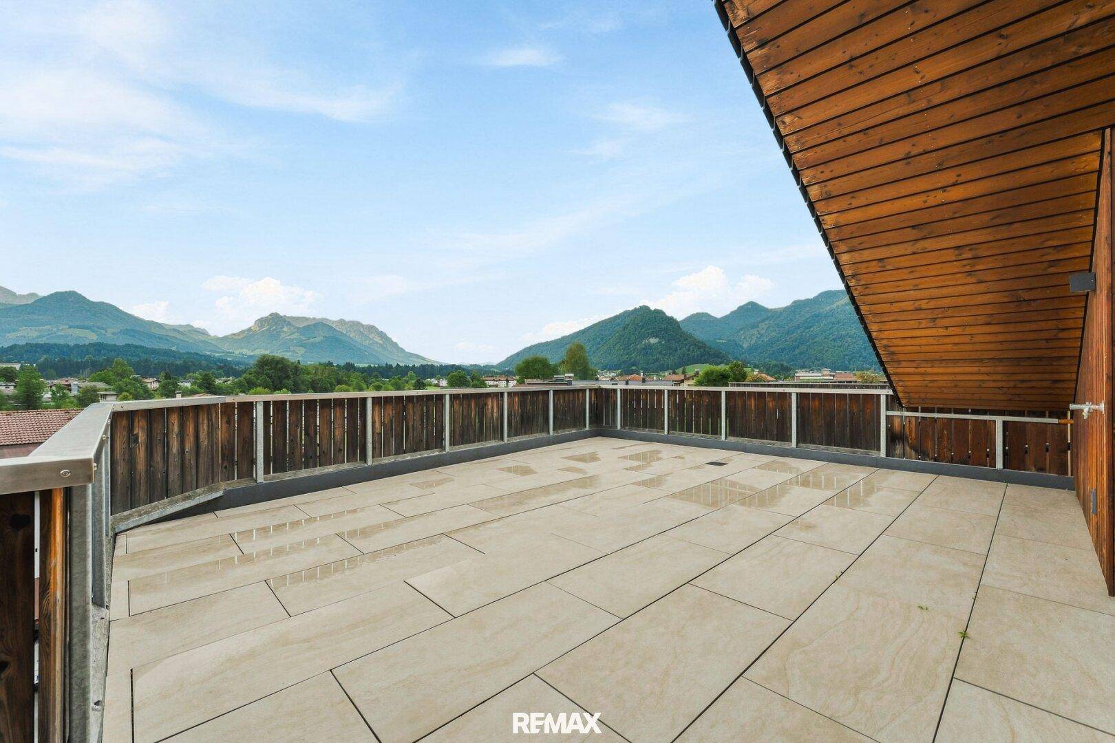 Weitläufige Terrasse mit Fliesenboden und Holzgeländer, umgeben von einer malerischen Bergkulisse.