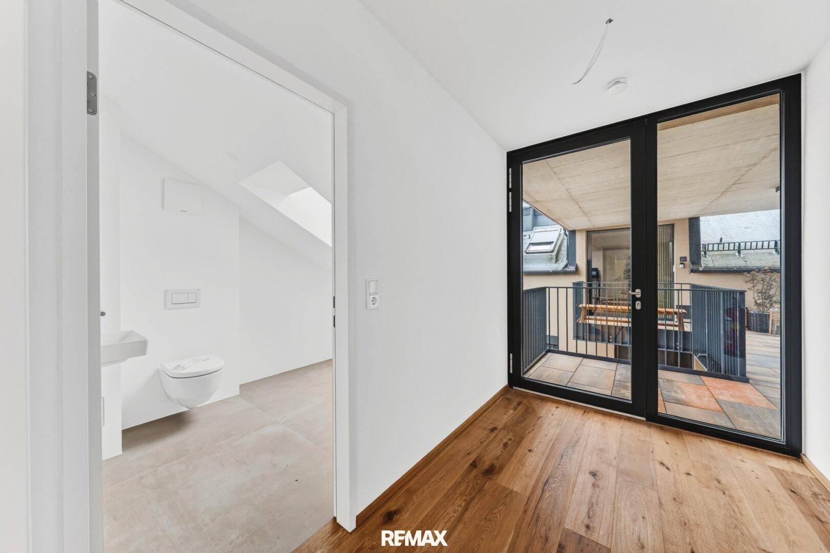 Helles Zimmer mit Holzboden und Zugang zu einem Balkon mit Bergblick.