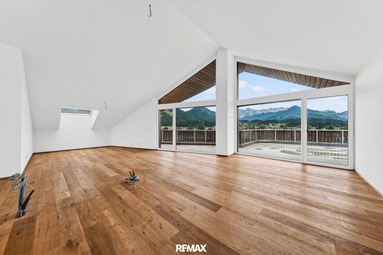 Weitläufiger Wohnbereich mit Holzboden, Dachschrägen und Zugang zu einer großen Terrasse.