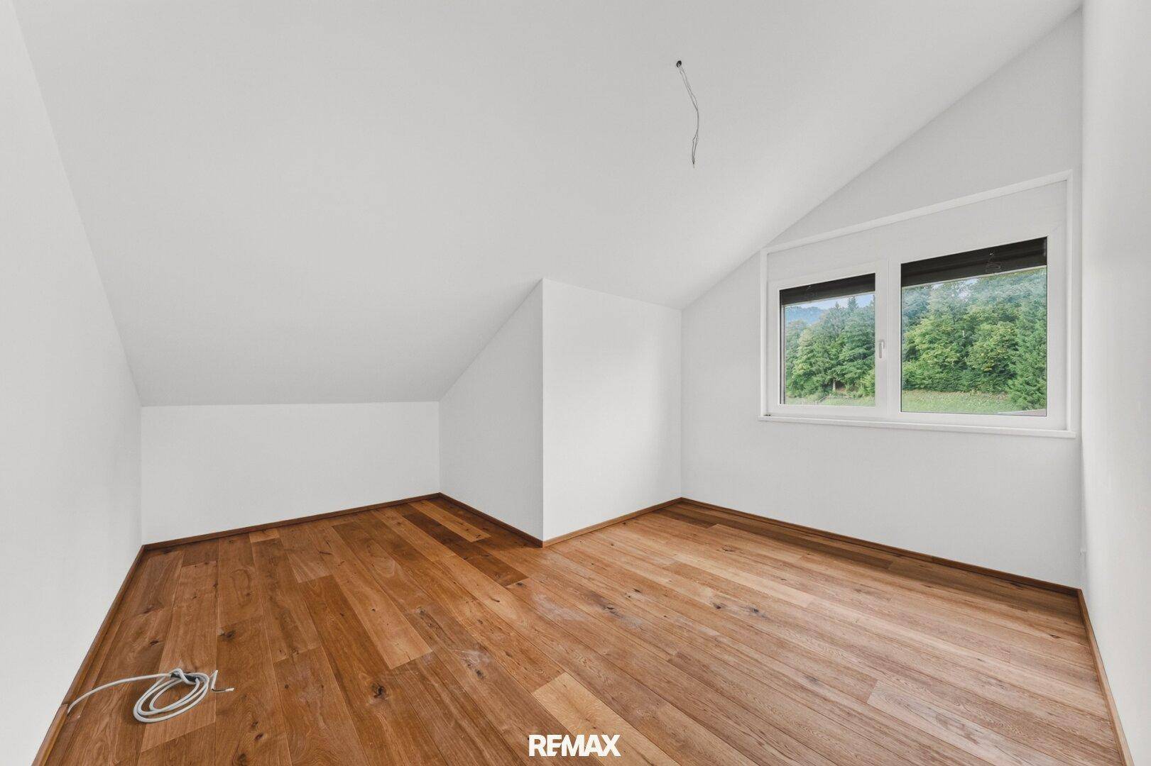 Gemütliches Schlafzimmer mit Holzboden, Dachschräge und Fenster mit Blick ins Grüne.