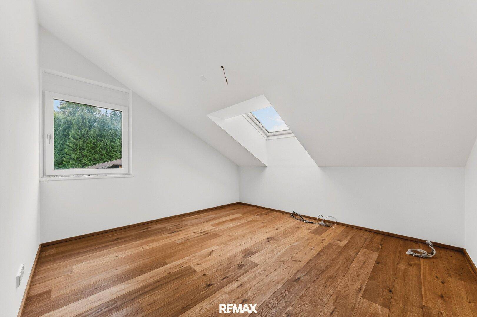 Helles Schlafzimmer mit Holzboden, Dachschräge und Oberlicht für zusätzliches Tageslicht.