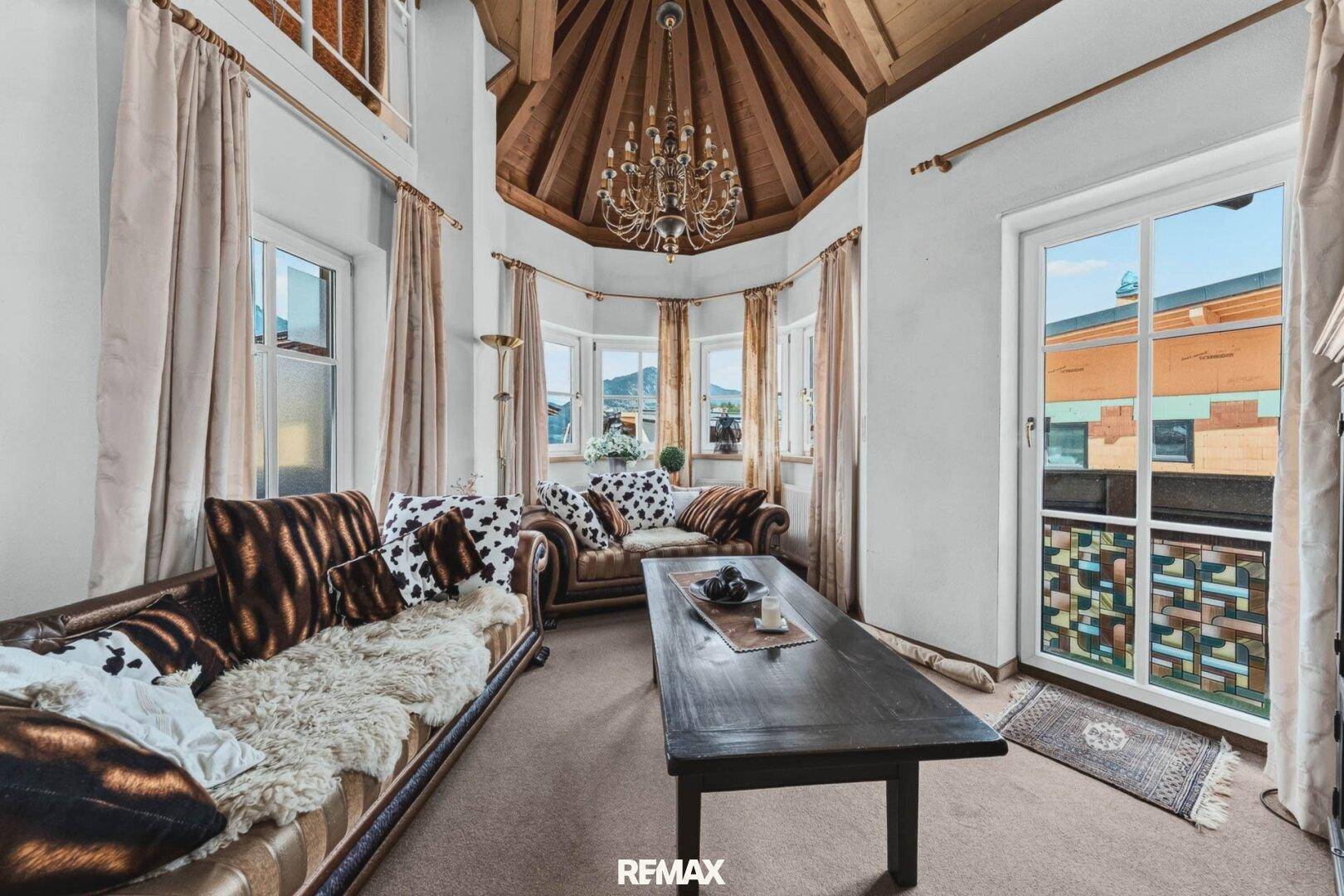 Wohnzimmer mit hoher Holzdecke, Kronleuchter und gemütlichen Sofas im alpinen Stil.