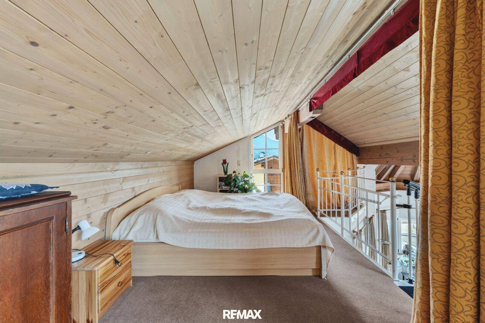Helles Schlafzimmer im Dachgeschoss mit Holzverkleidung und schrägen Wänden.