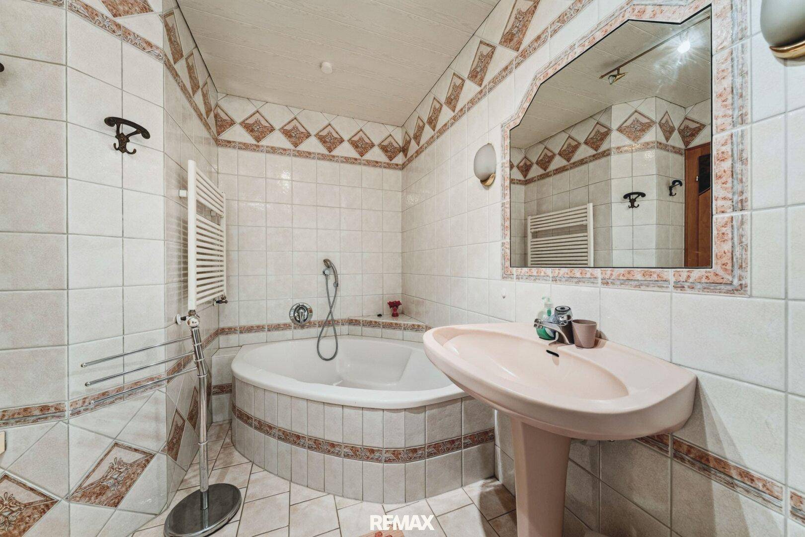 Badezimmer mit Eckbadewanne, Fliesen im 80er-Jahre-Stil und beheiztem Handtuchhalter.