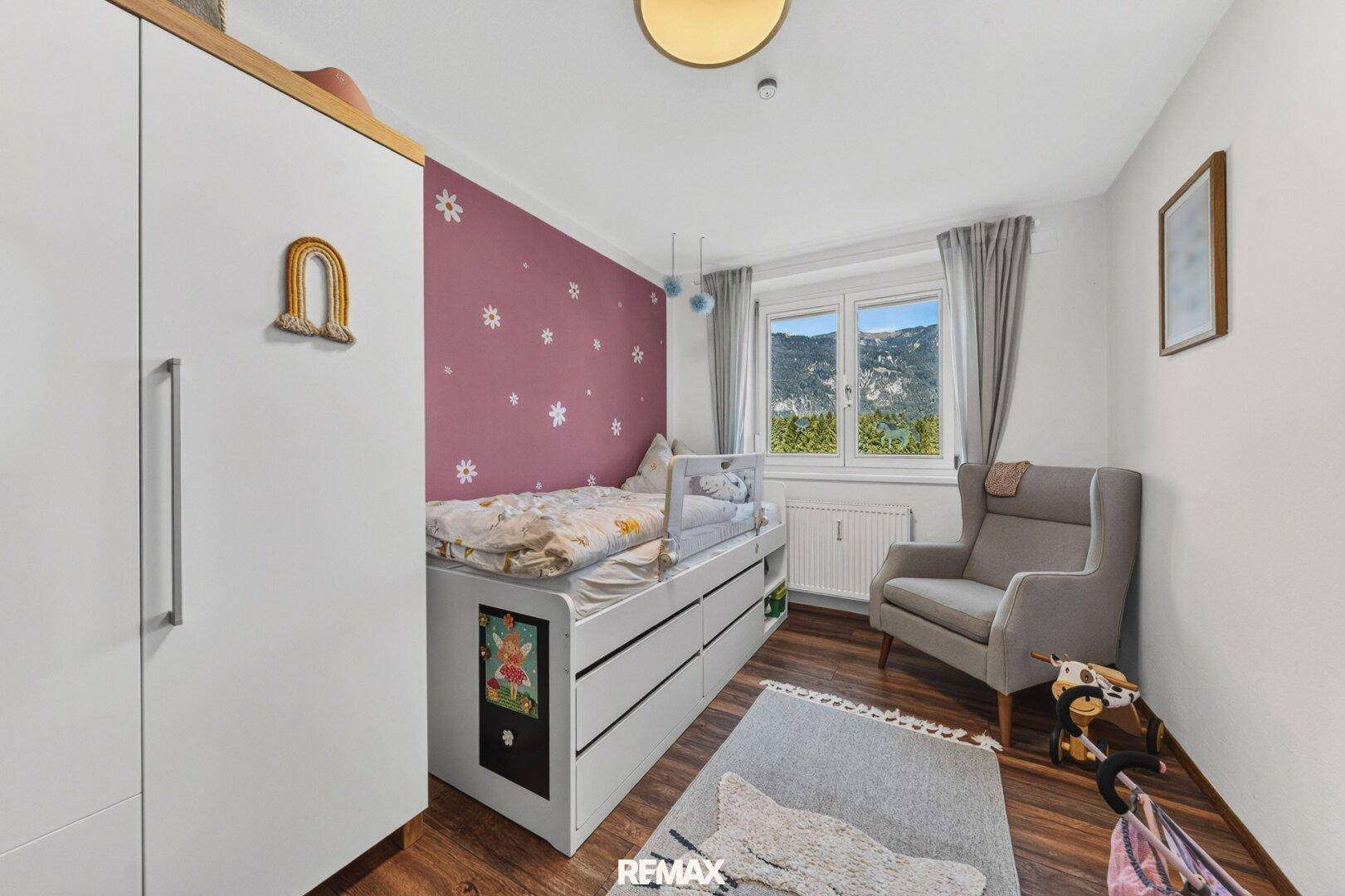 Kinderzimmer mit Einzelbett, Schrank und Blick ins Grüne.