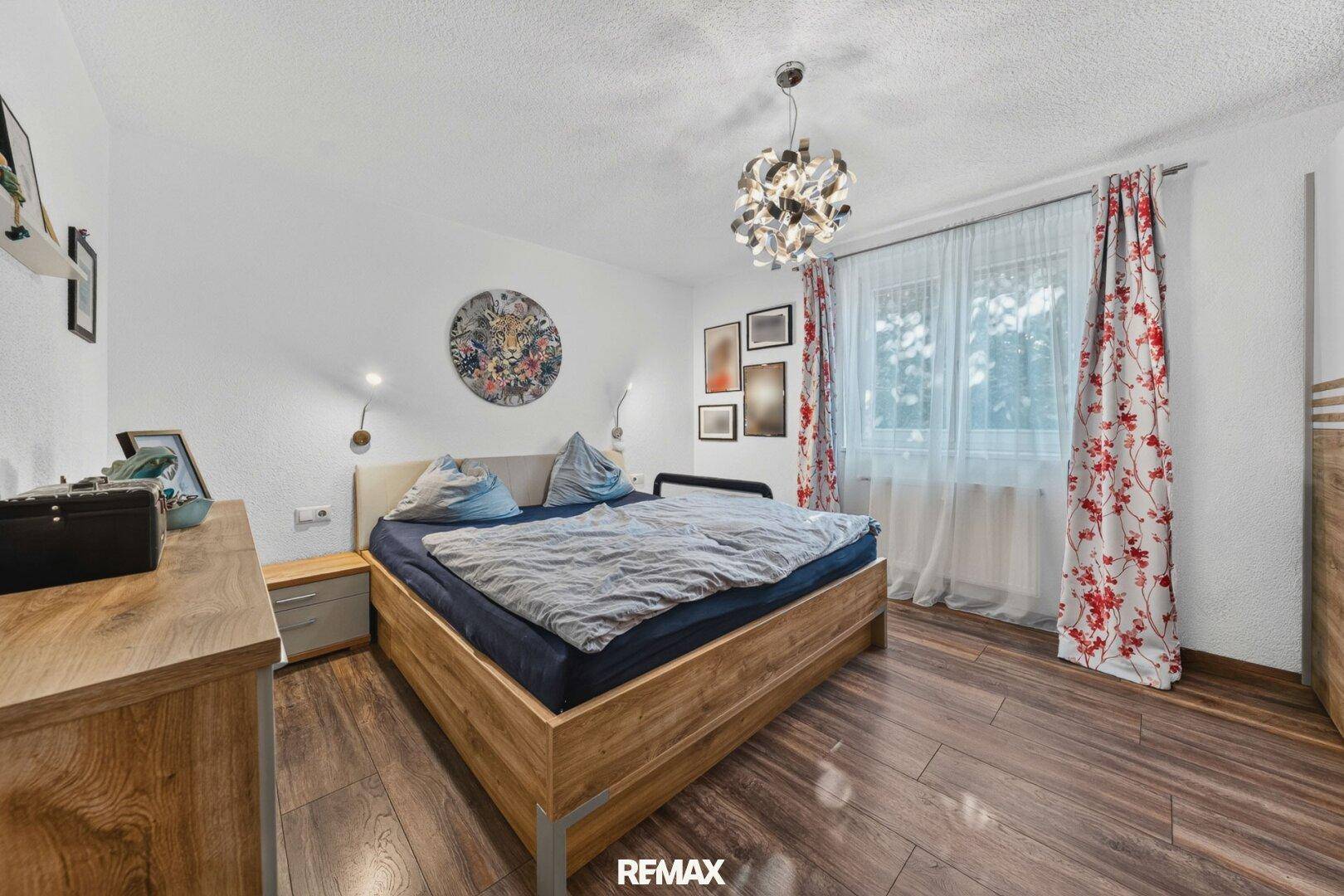 Gemütliches Schlafzimmer mit Holzbett, dunklem Holzboden und floralen Vorhängen.