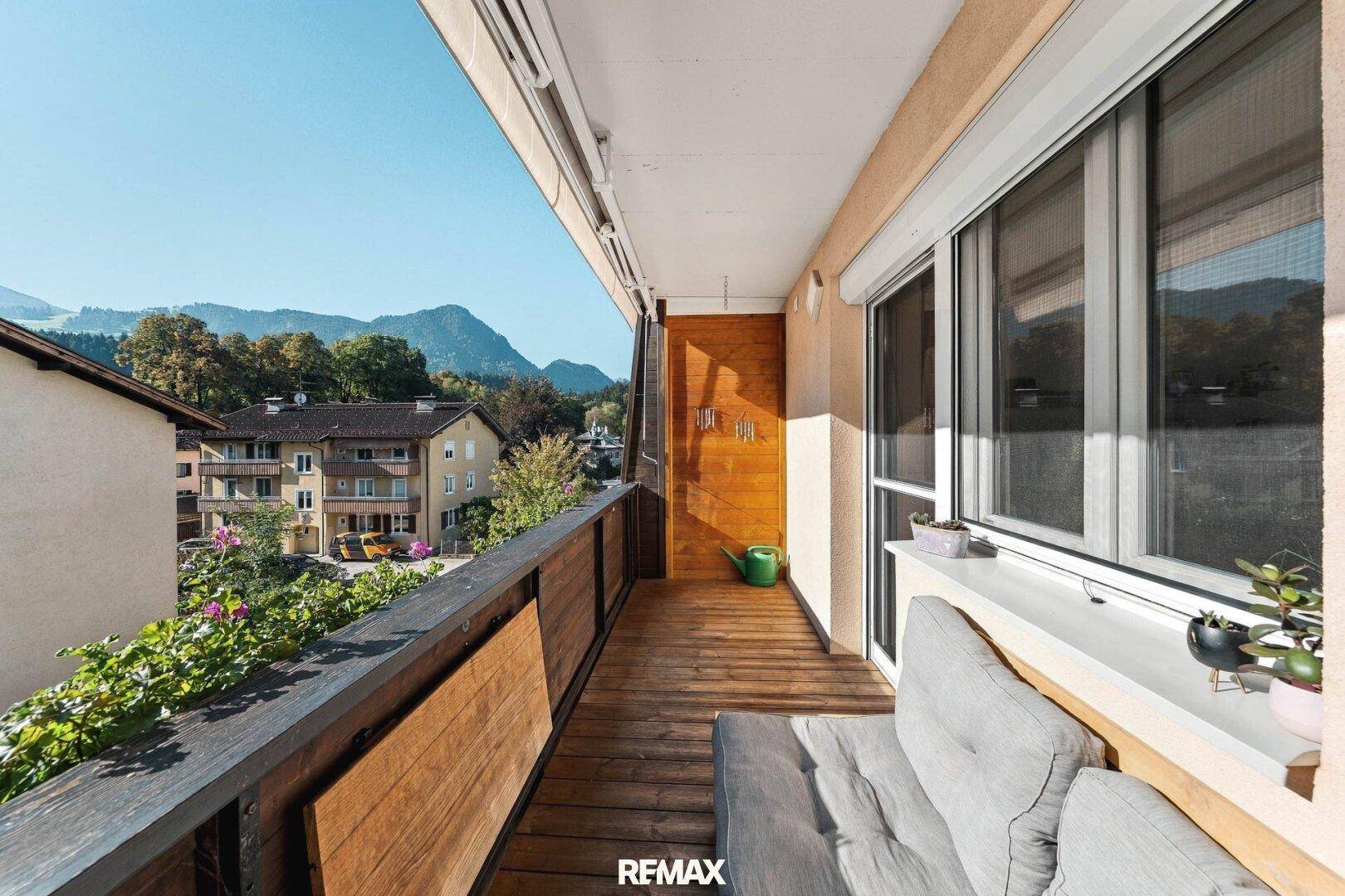 Langer Balkon mit Holzboden, Sitzgelegenheit und Bergblick.
