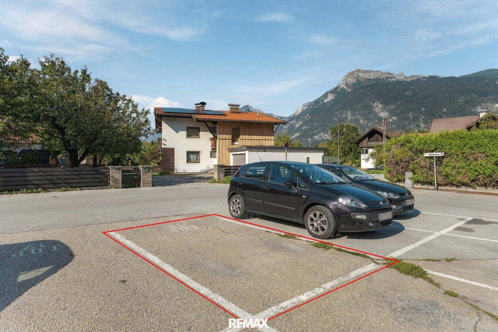 Außenparkplatz mit markierter Stellfläche vor einer Wohnanlage mit Bergblick.