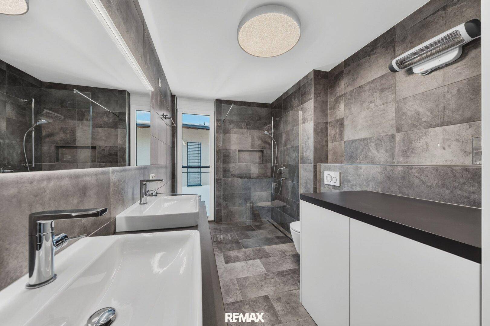 Modernes Badezimmer mit doppelten Waschbecken, großer Dusche und grauen Fliesen.