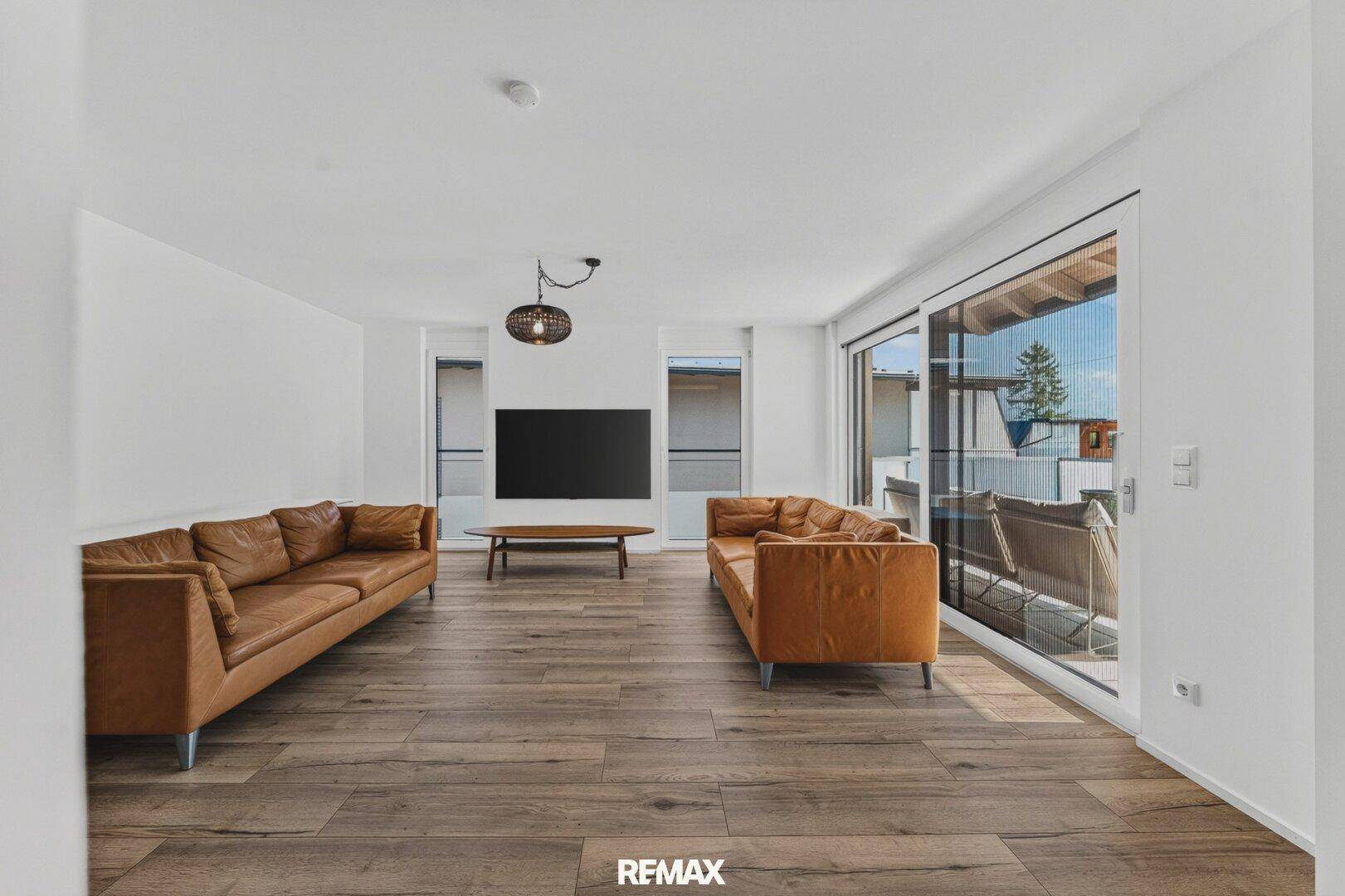 Geräumiges Wohnzimmer mit zwei Ledersofas, großem Fernseher und Zugang zur Terrasse.