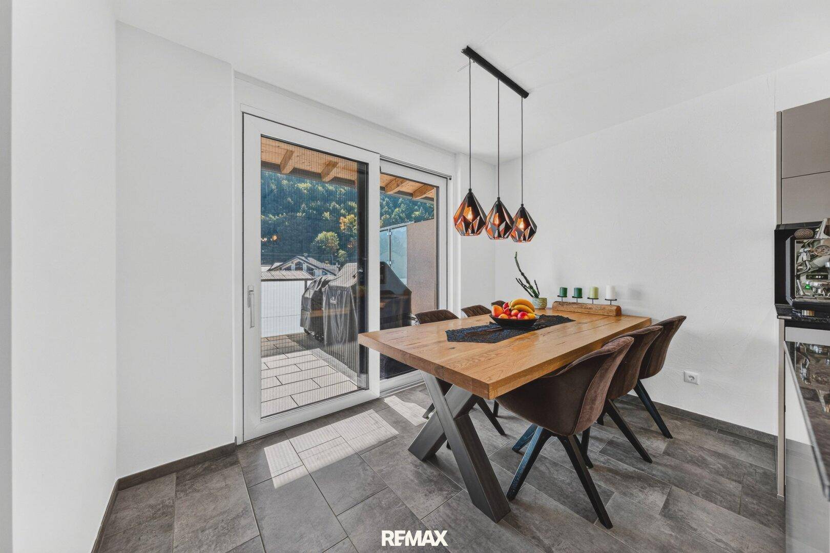 Heller Essbereich mit Holztisch, modernen Pendelleuchten und Zugang zur Terrasse.