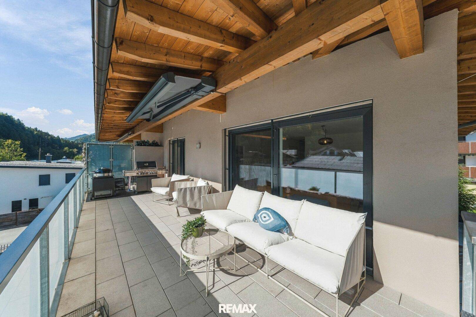 Große möblierte Terrasse mit Holzdach, Grillbereich und Bergblick.