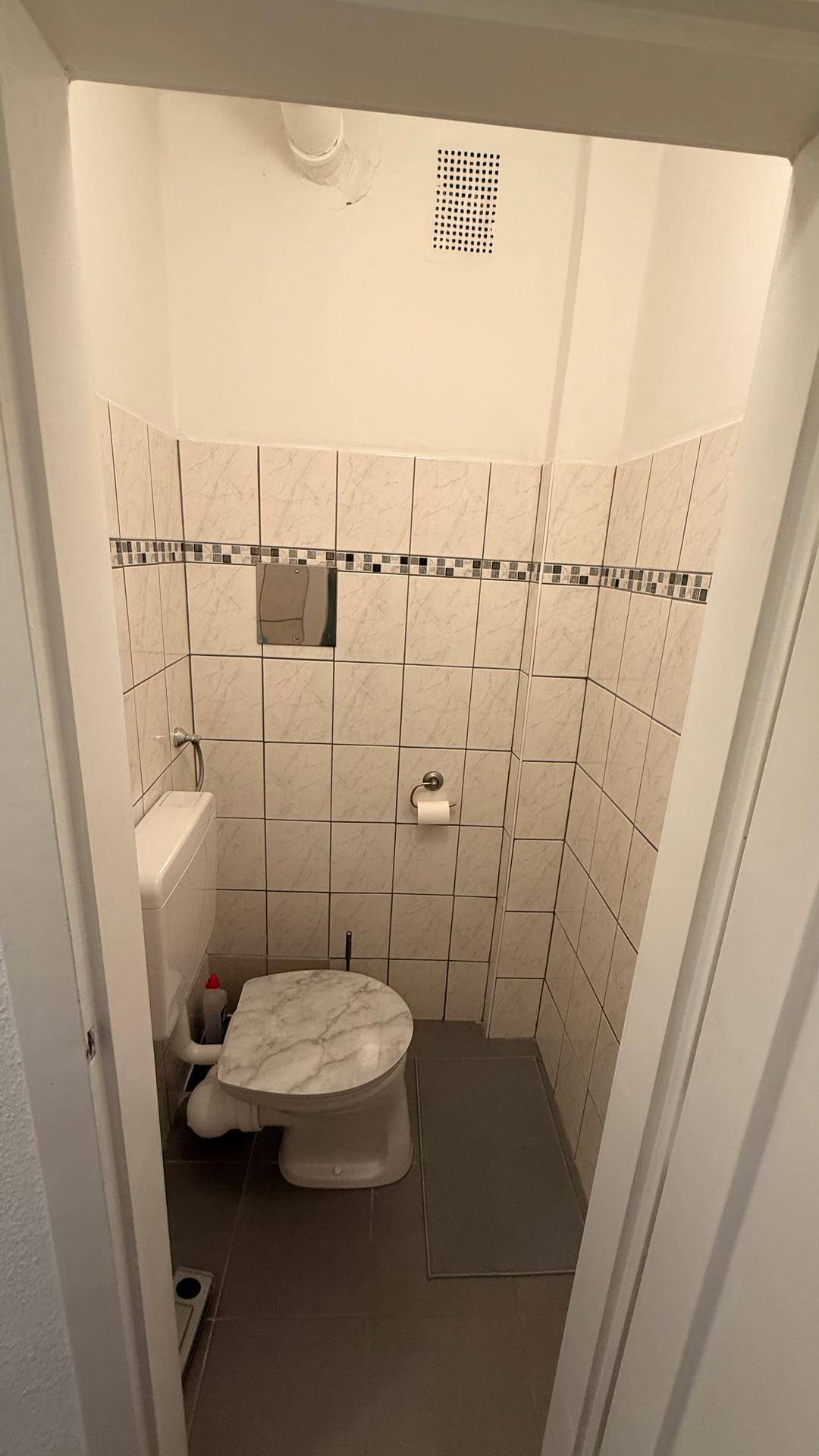 Separate Toilette mit WC, Waschbecken und hellen Fliesen an den Wänden.