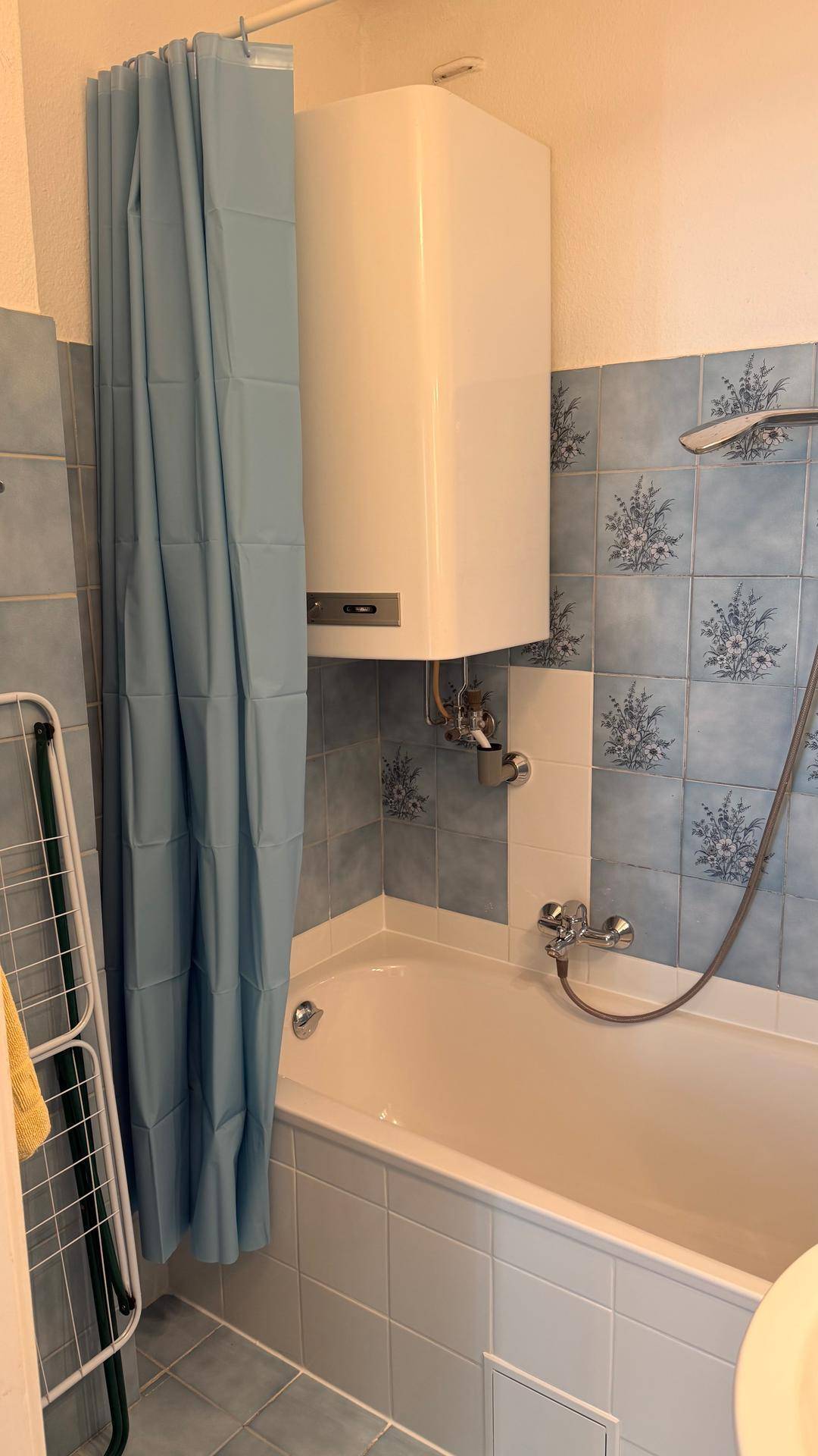 Badezimmer mit Badewanne, Duschvorhang und einem Warmwasserbereiter an der Wand.