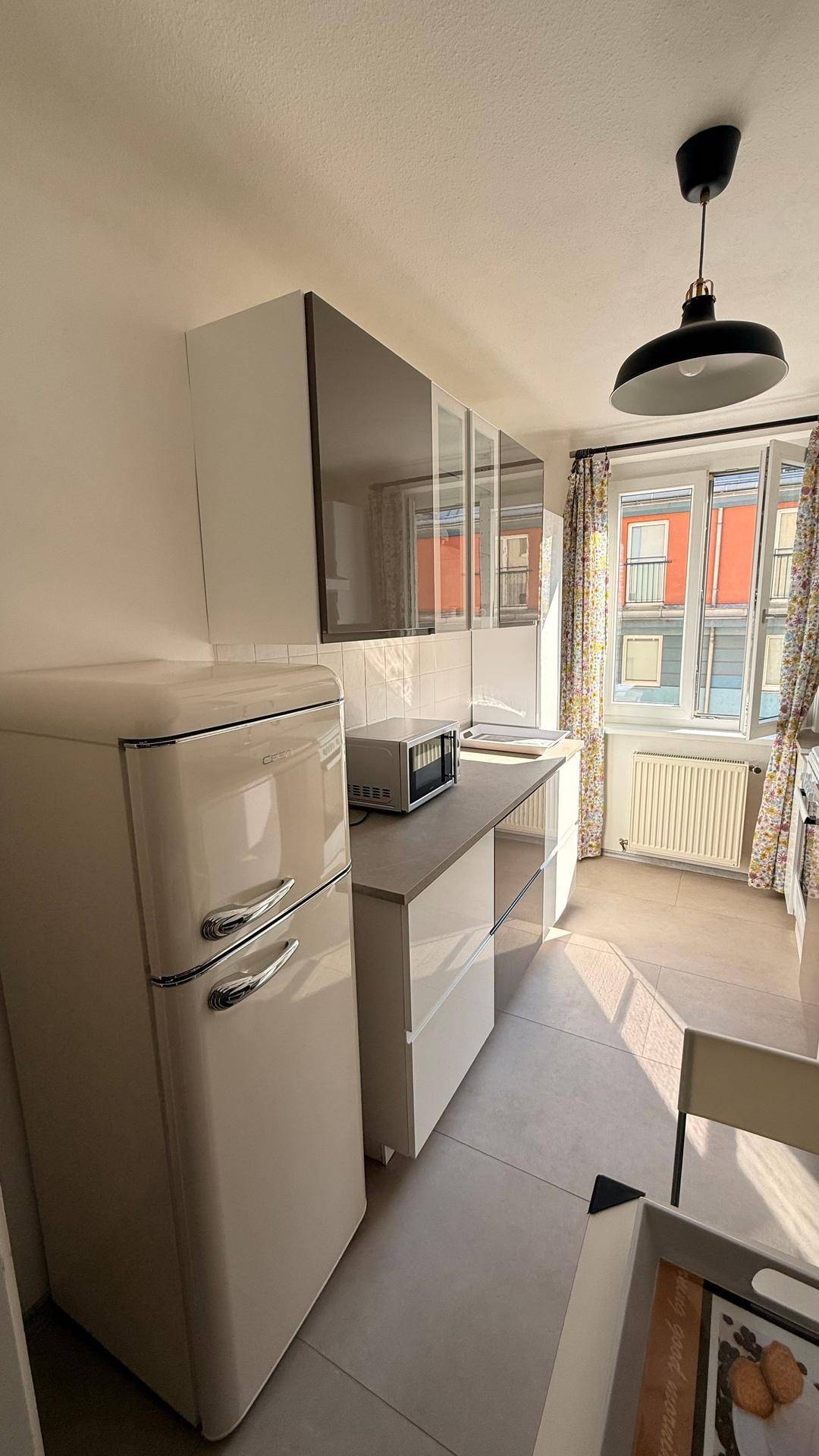 Küche mit Retro-Kühlschrank, weißen Schränken und einem Fenster mit Blick nach draußen.