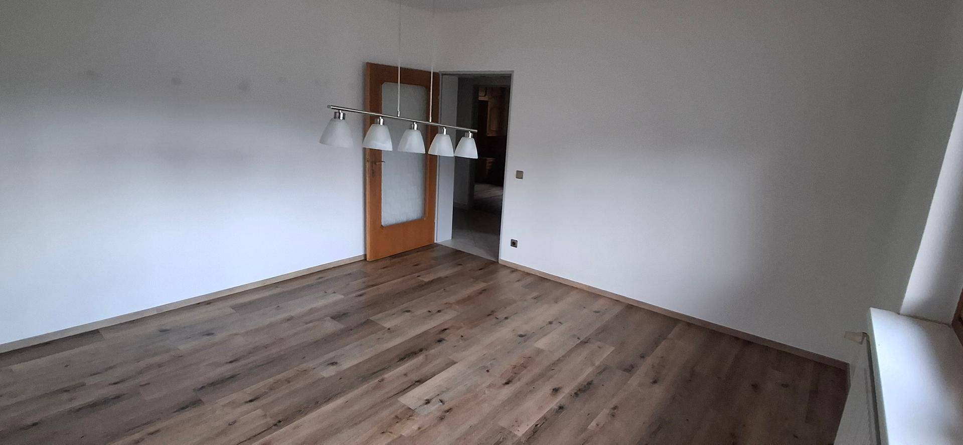 Geräumiges Wohnzimmer mit Laminatboden und moderner Deckenleuchte, bereit zur Einrichtung.