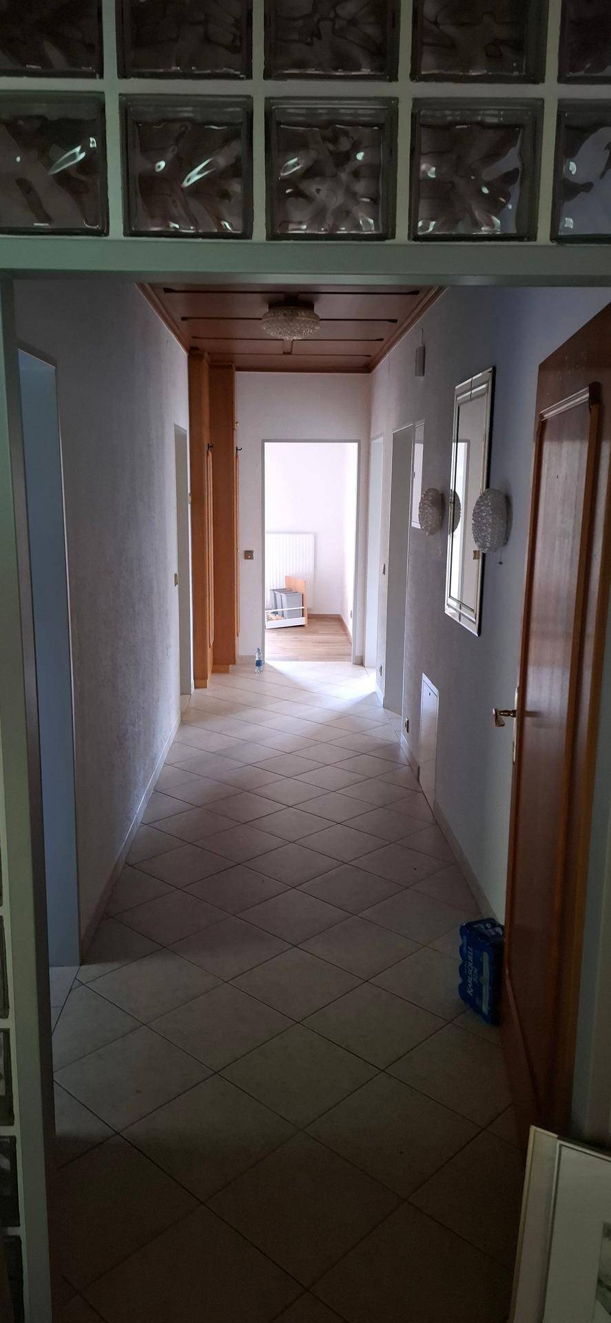 Flur mit Fliesenboden und Holztäfelung an der Decke, der zu verschiedenen Bereichen führt.