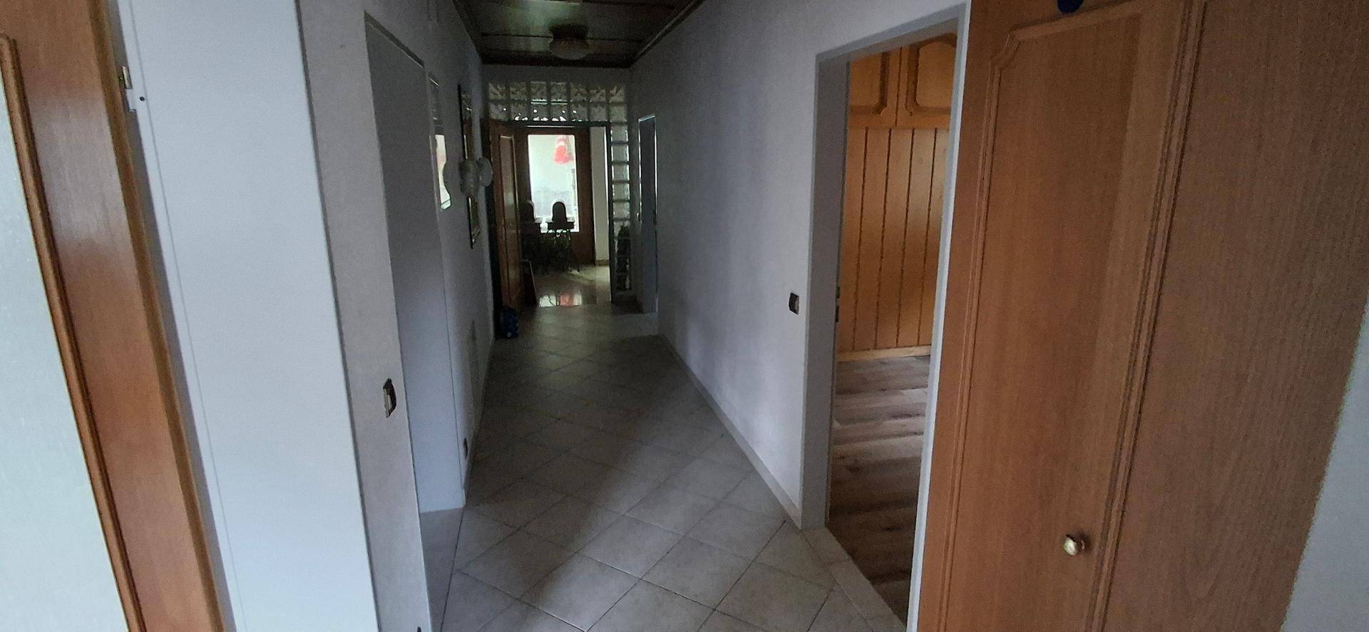 Langer Flur mit Fliesenboden und Holztäfelung an der Decke, der verschiedene Räume verbindet.