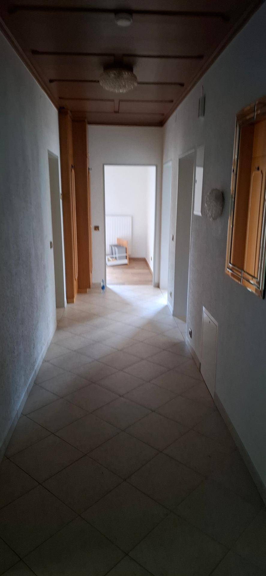 Langer Flur mit Fliesenboden und Holztäfelung an der Decke, der zu weiteren Räumen führt.